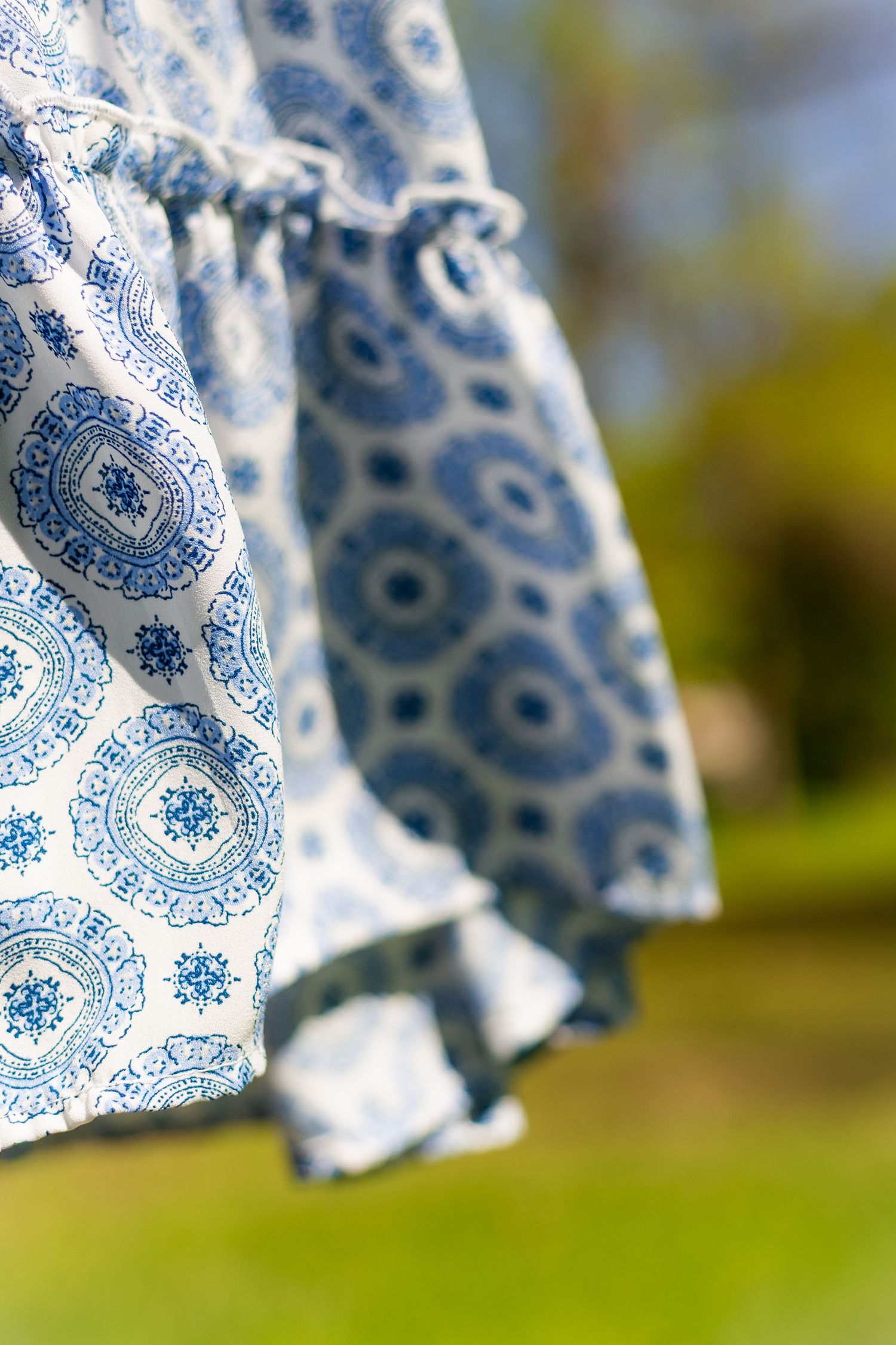 Close-up of flowing blue and white geometric patterned dress skirt in outdoor natural setting.
