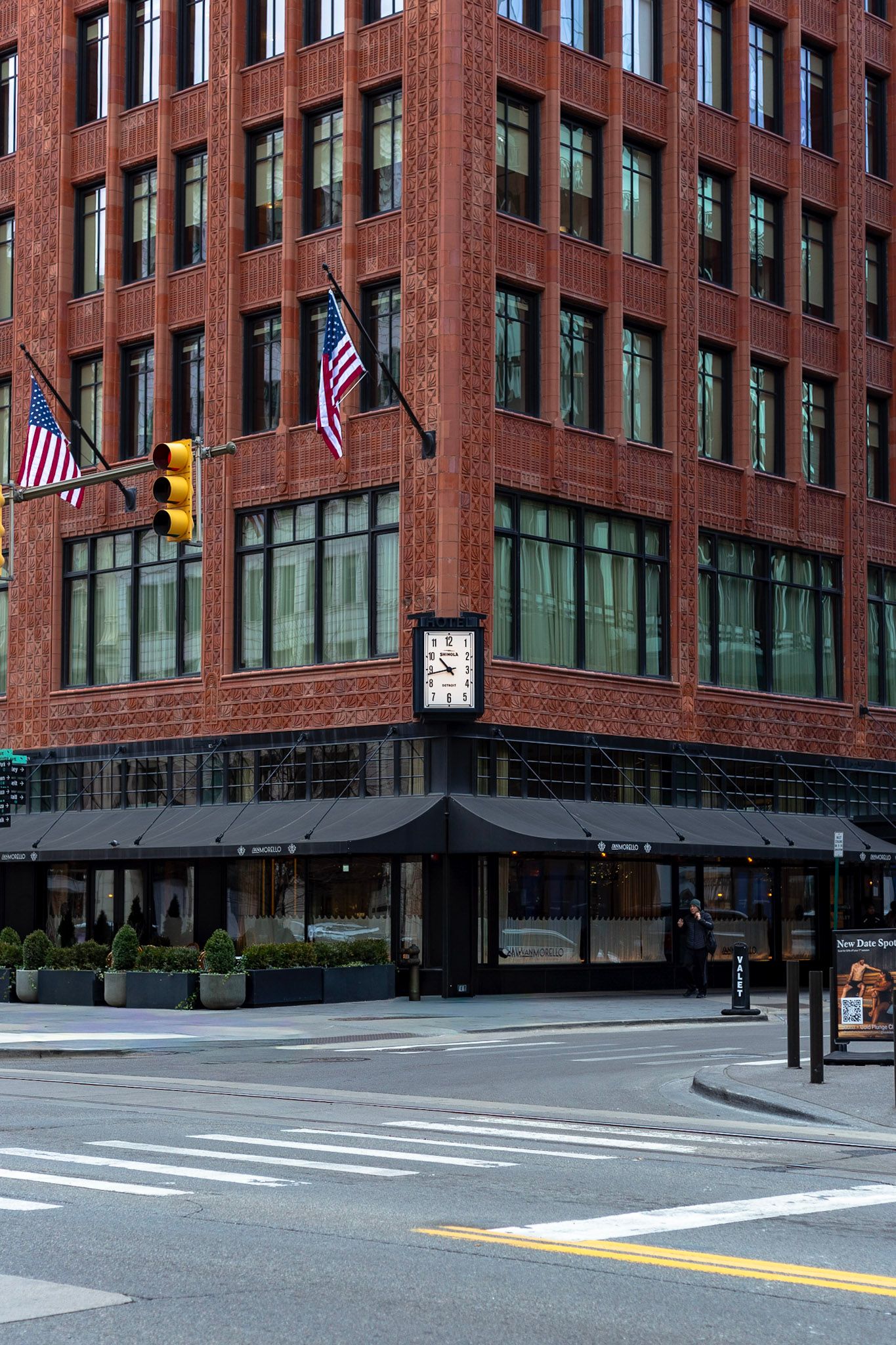 Corner of a red brick building with American flags, street clock, and black awning at an intersection.