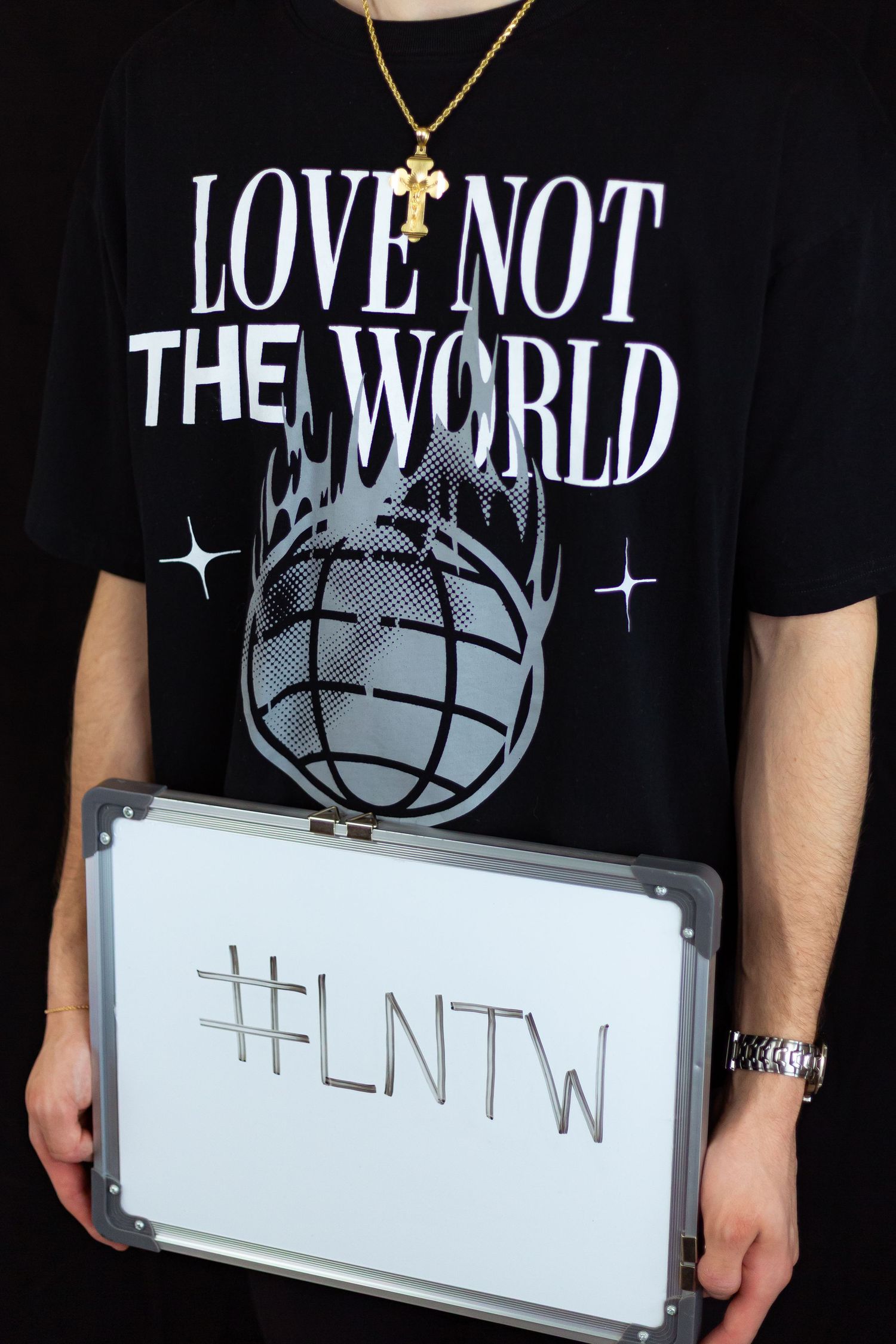 Person holding #LNTW whiteboard wearing black Love Not The World t-shirt with gold cross necklace.