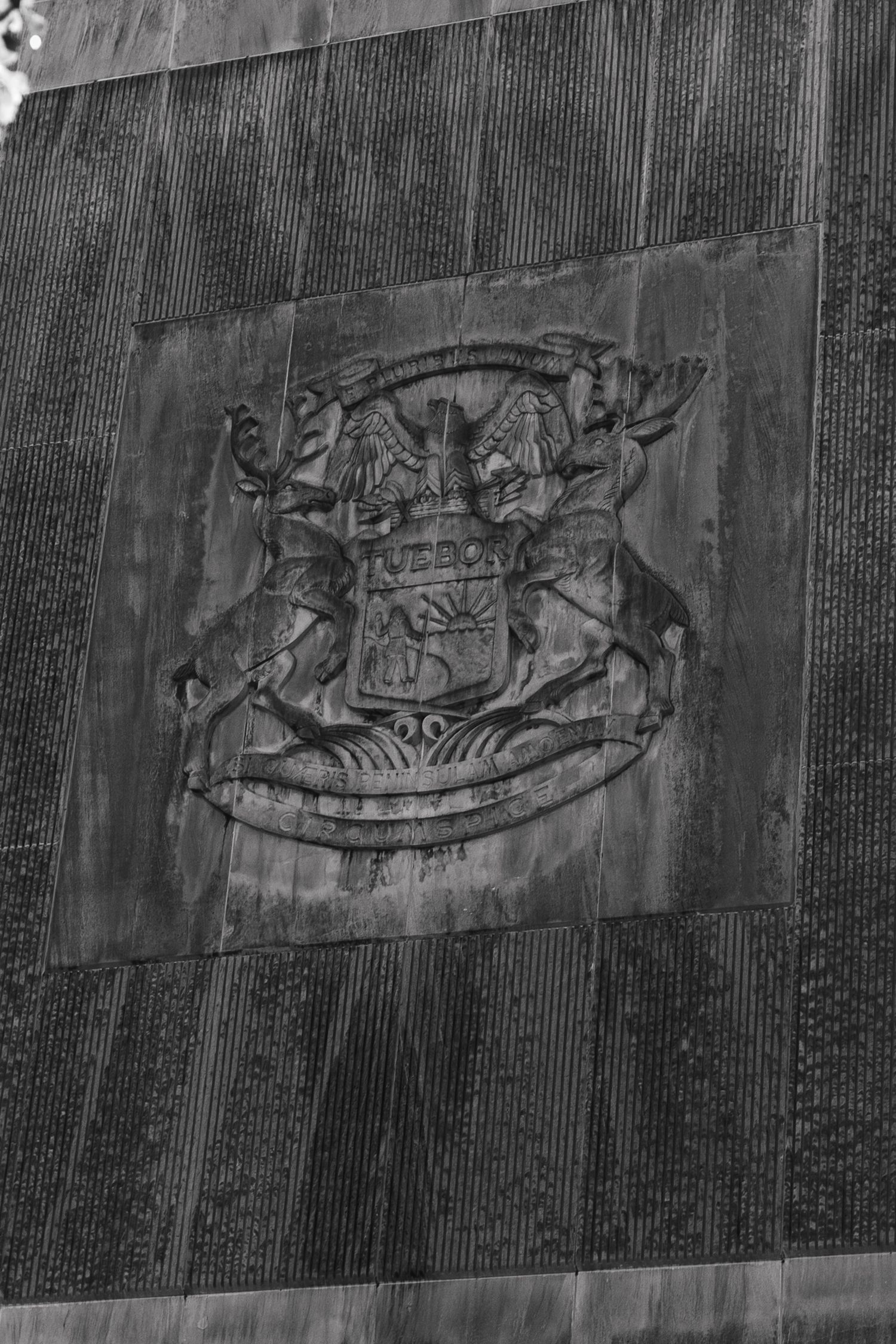 Black and white photo of an ornate coat of arms relief sculpture on a building exterior wall.