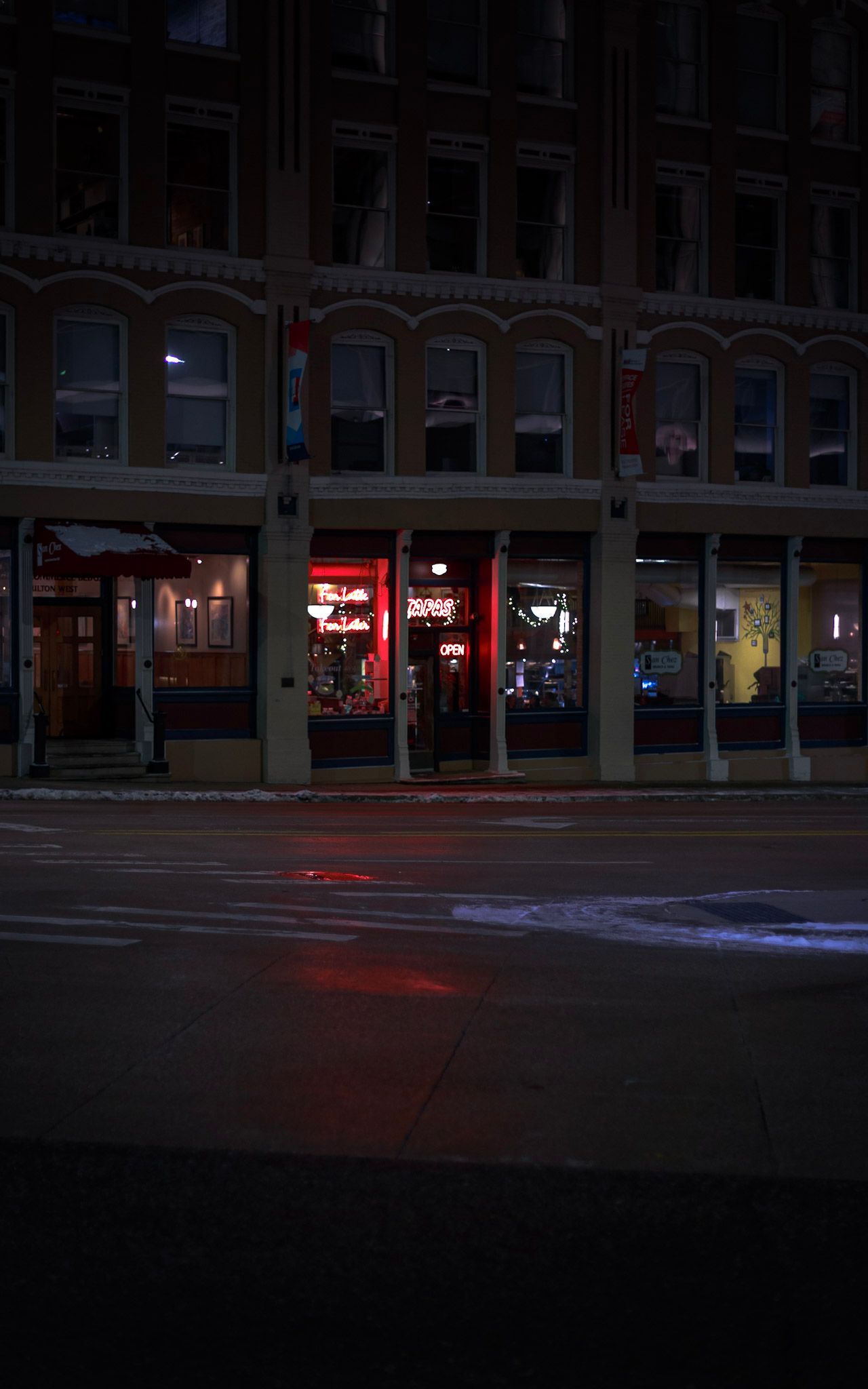 Dark urban street corner at night with neon red lights glowing from a storefront.