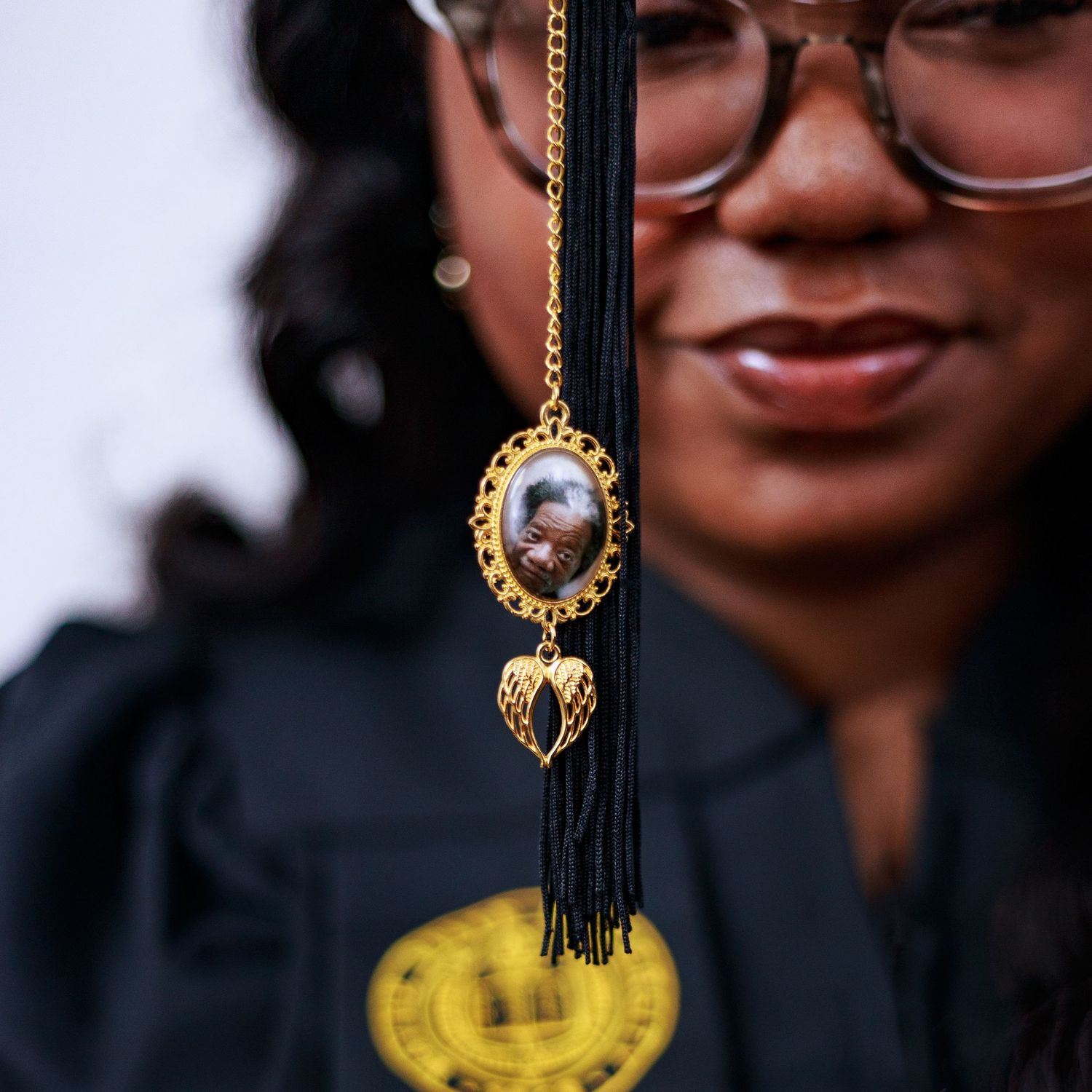 Close-up of a gold ornate graduation tassel charm with a memorial photo pendant on a black graduation cap tassel.