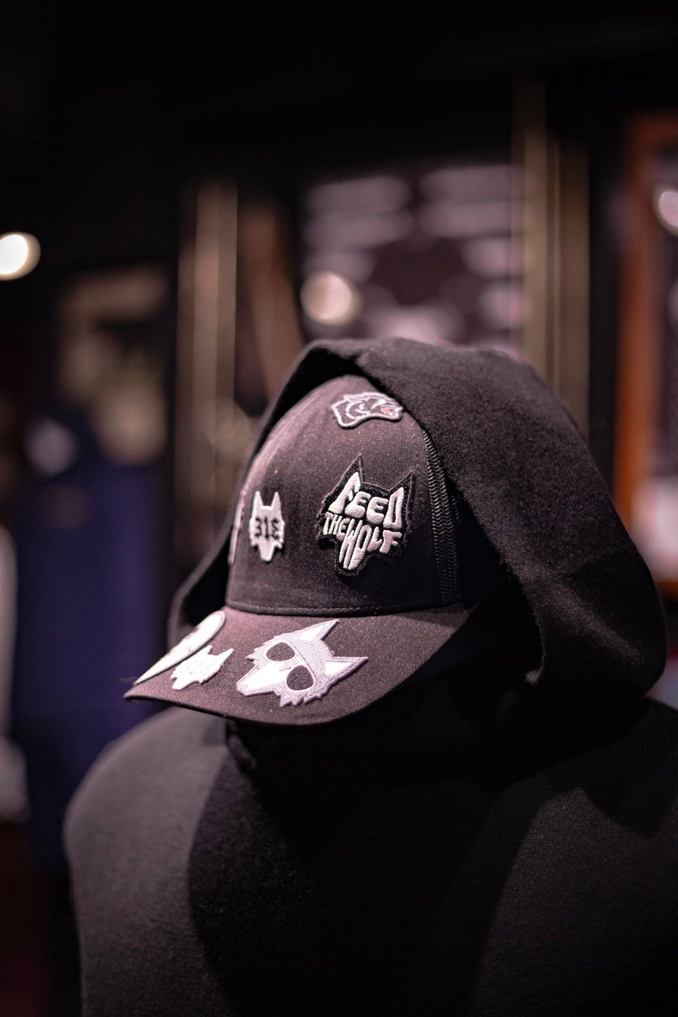 Black snapback cap with Feed the Wolf and 313 embroidered patches on a hooded mannequin in a dark store.