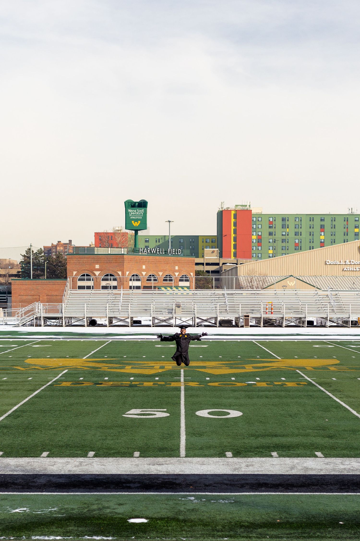 Wayne State University graduate stands at the 50-yard line of the snow-dusted campus football field.