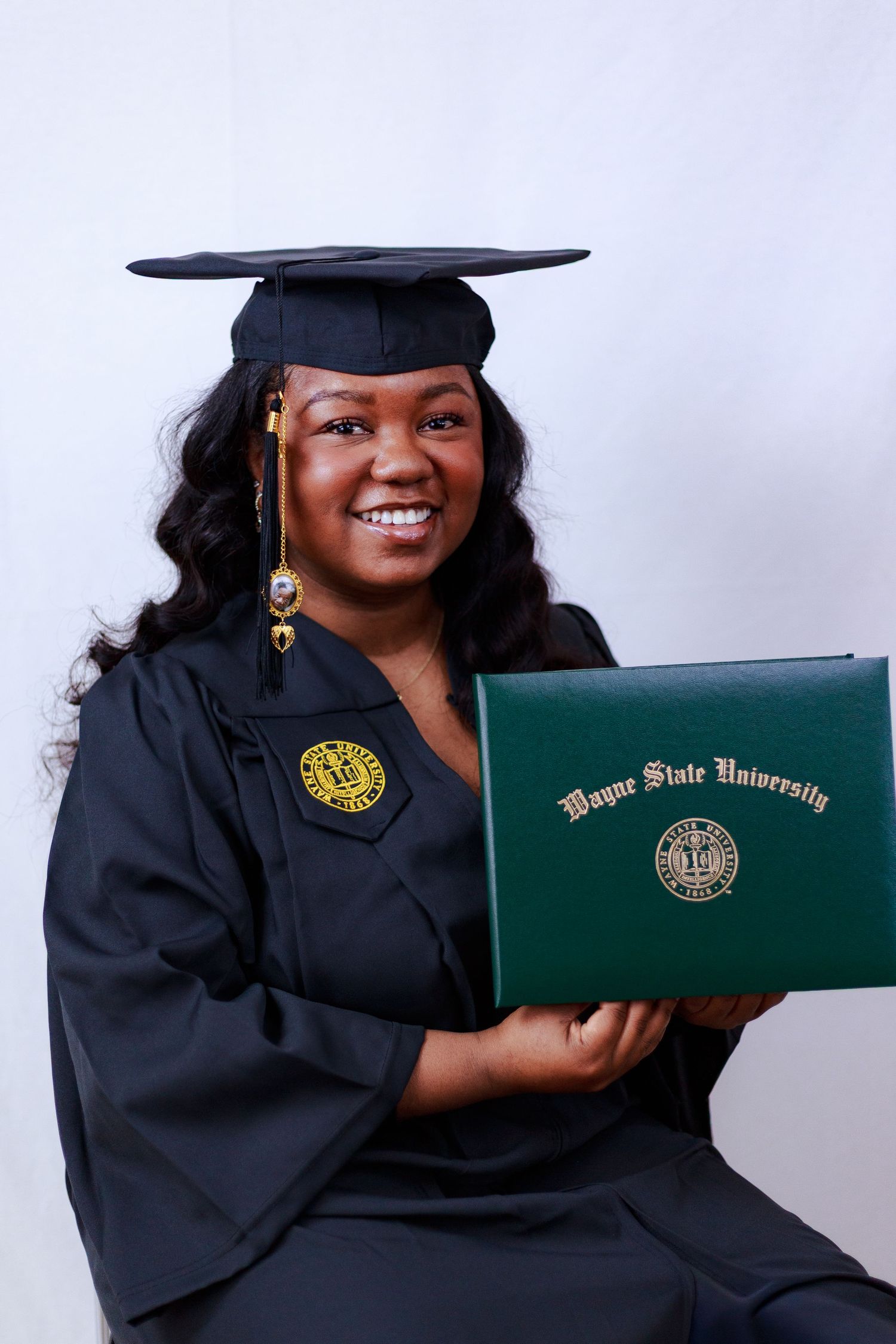 Proud Wayne State University graduate in black cap and gown holding green diploma cover while smiling for photos.