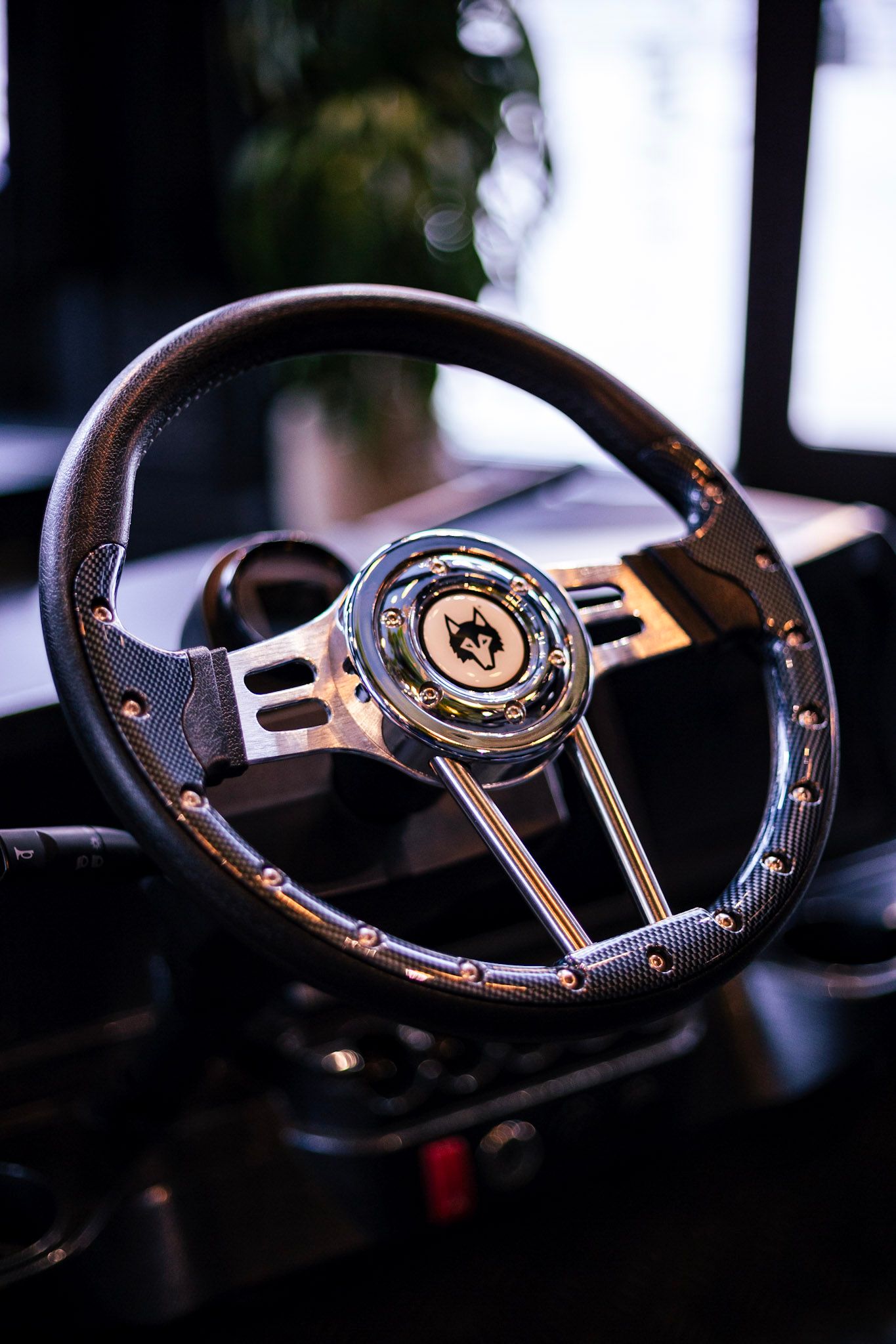 Vintage custom black leather steering wheel with chrome hub featuring a wolf logo emblem detail.