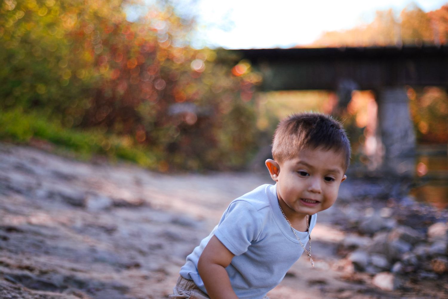 Smiling toddler boy crawling on sandy ground outdoors during autumn with bokeh background.