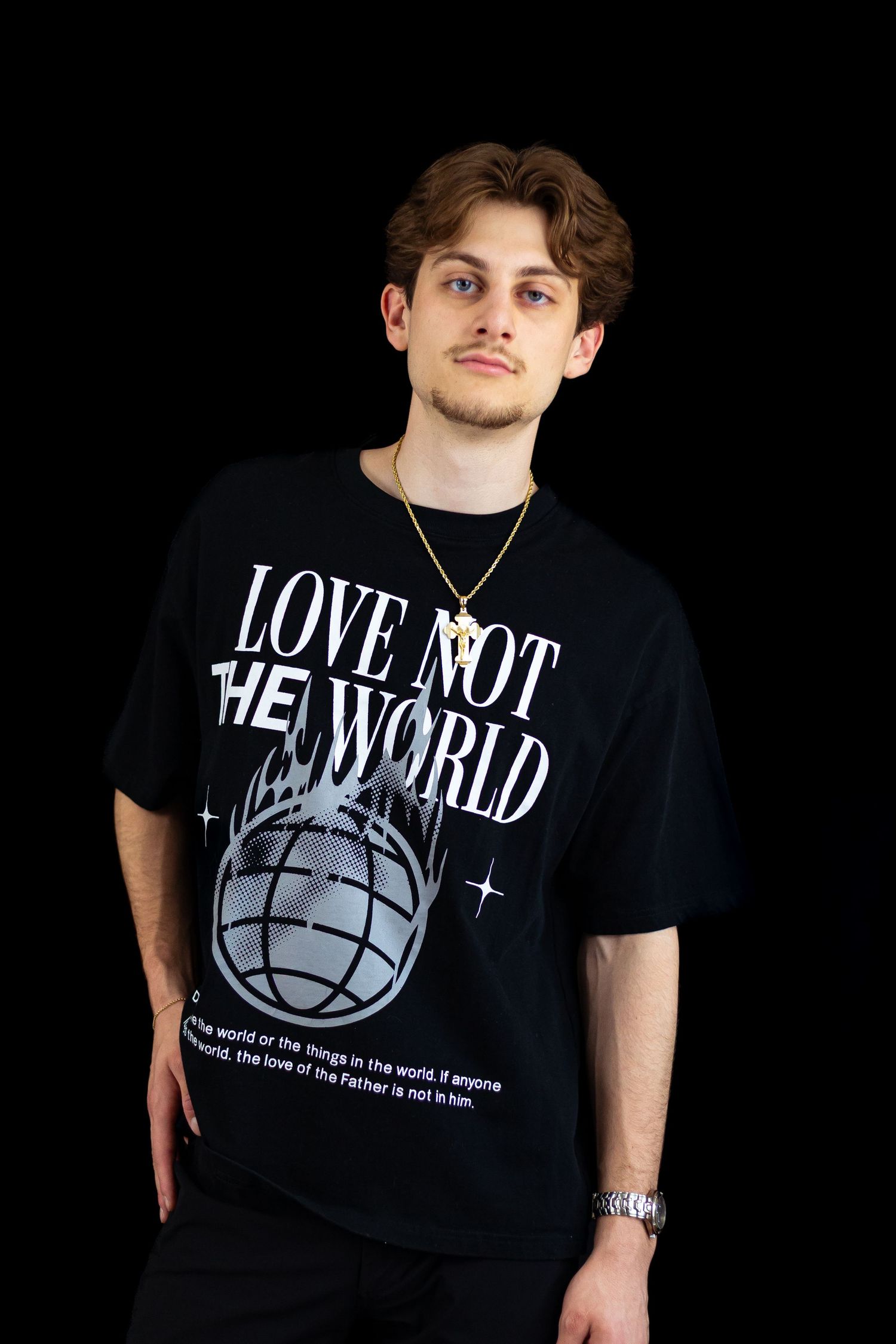 Young man in an oversized black Love Not The World graphic tee poses against a dark studio background.