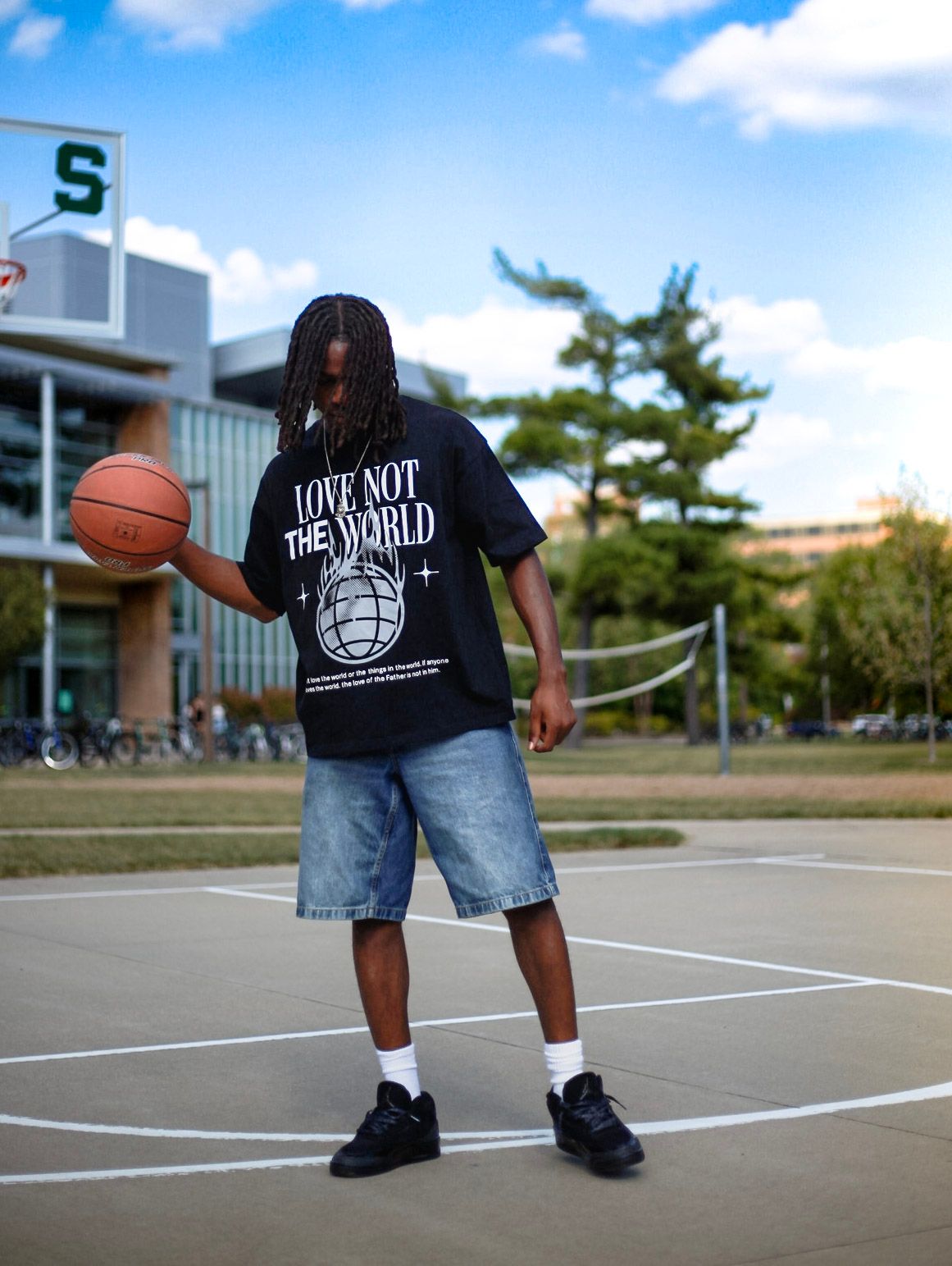 Man spinning basketball wearing black Love Not The World tee on outdoor court.