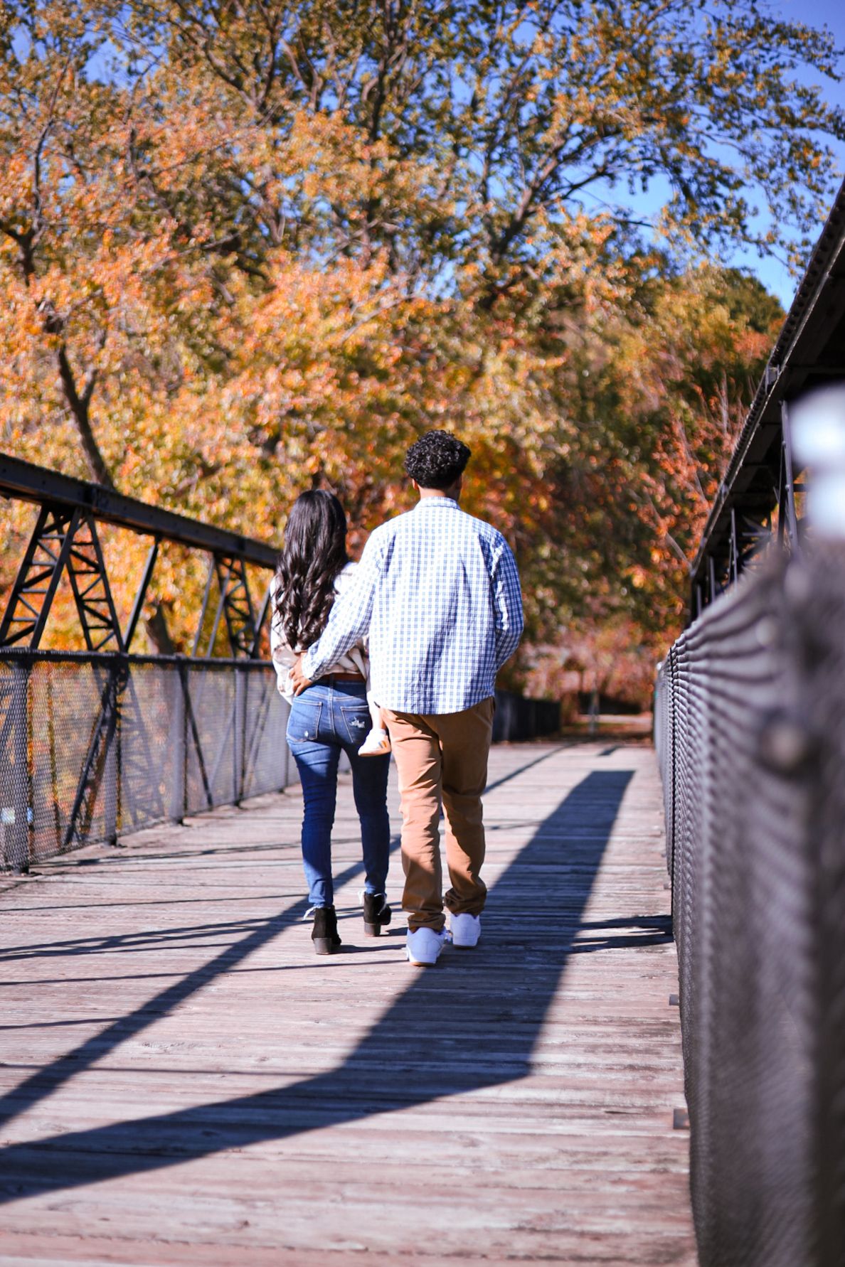 Couple walking hand-in-hand across a wooden bridge surrounded by vibrant fall foliage.