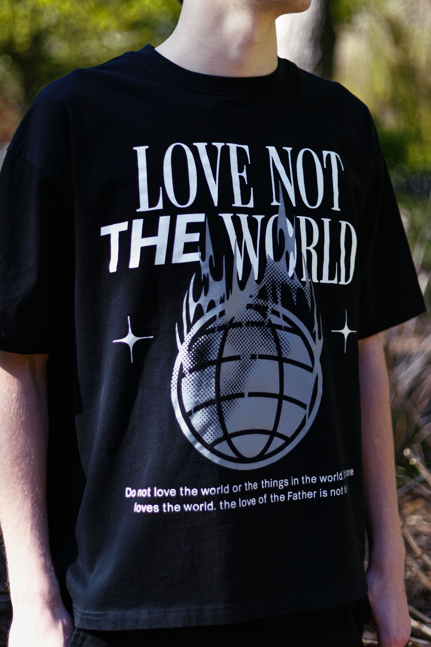 Close-up of black Love Not The World graphic t-shirt with globe and flame design with scripture text.