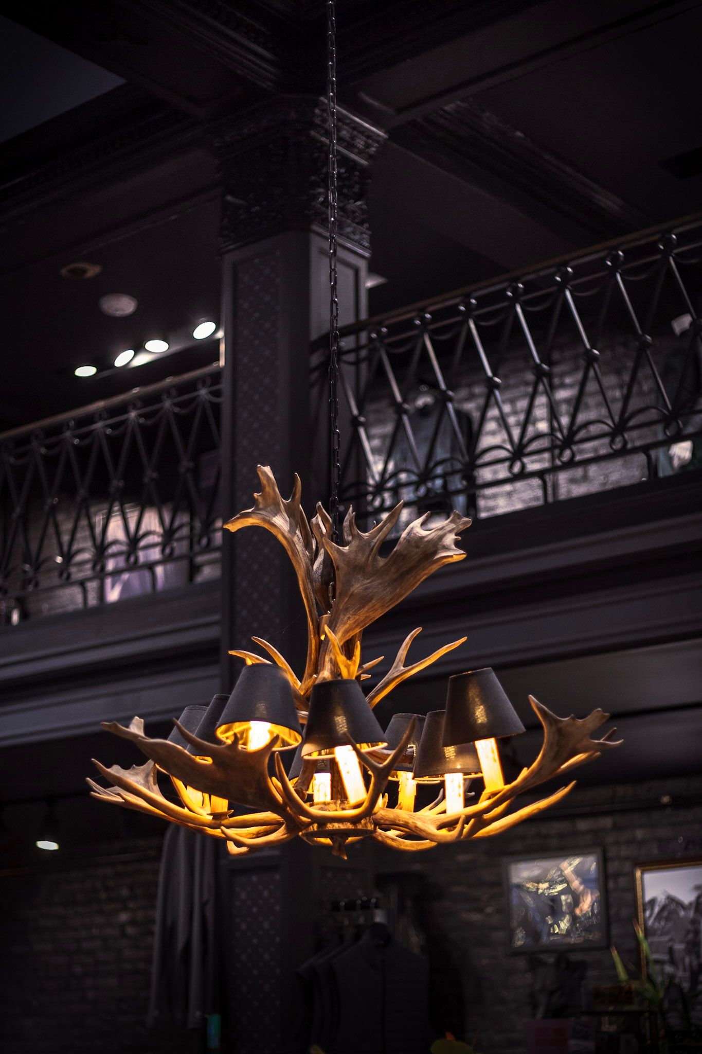 Rustic antler chandelier with black lamp shades hanging in a dark industrial interior.