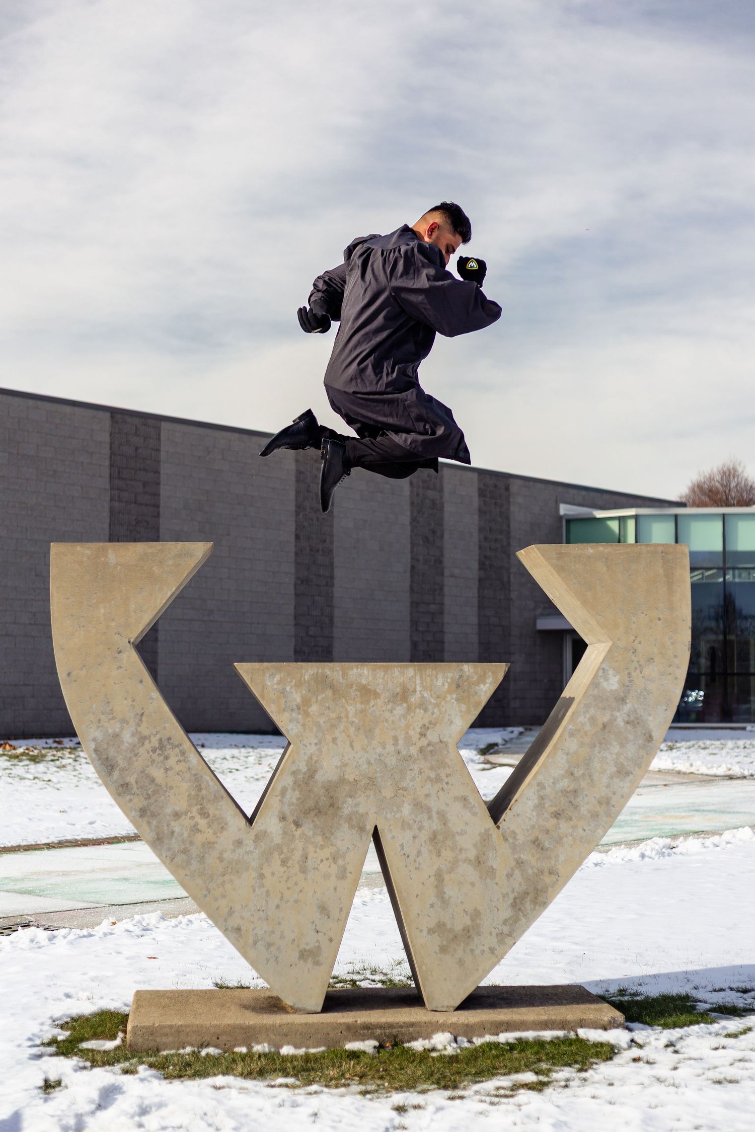 Man jumping over a large W sculpture on a snowy campus.