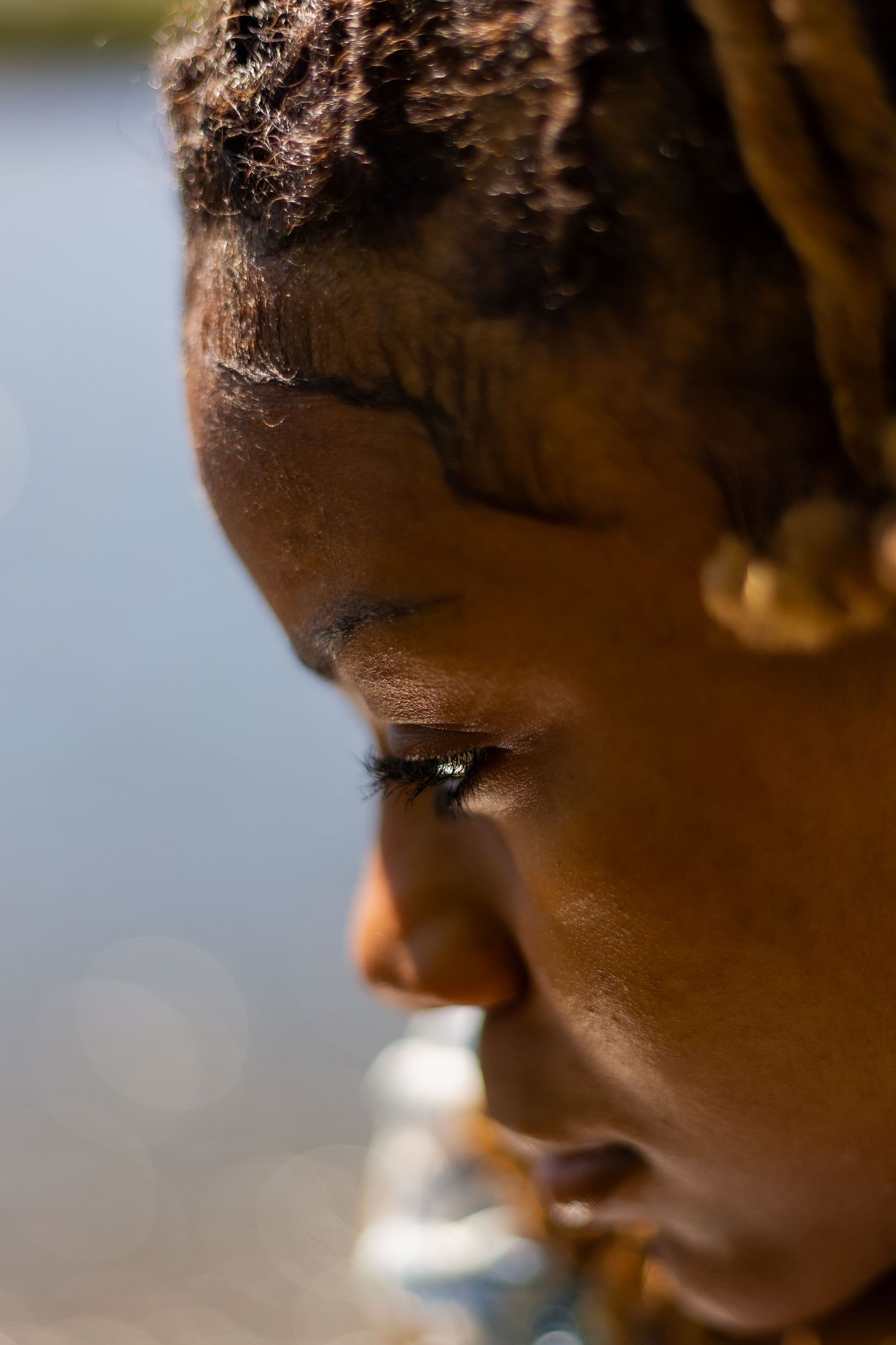 Close-up side profile of young Black woman with locs in natural sunlight outdoors.