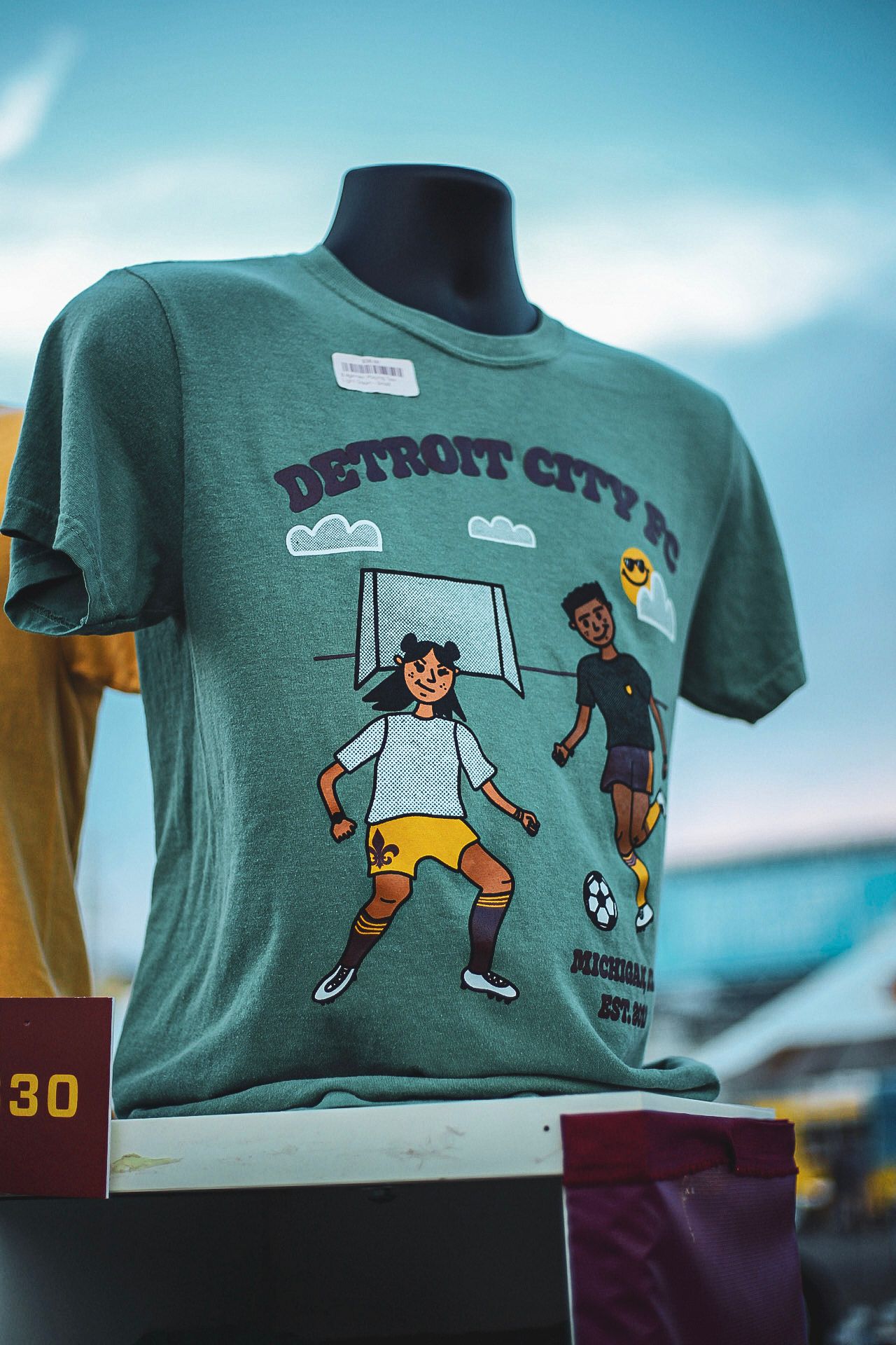 Green Detroit City FC merchandise t-shirt on mannequin displaying soccer players graphic design.