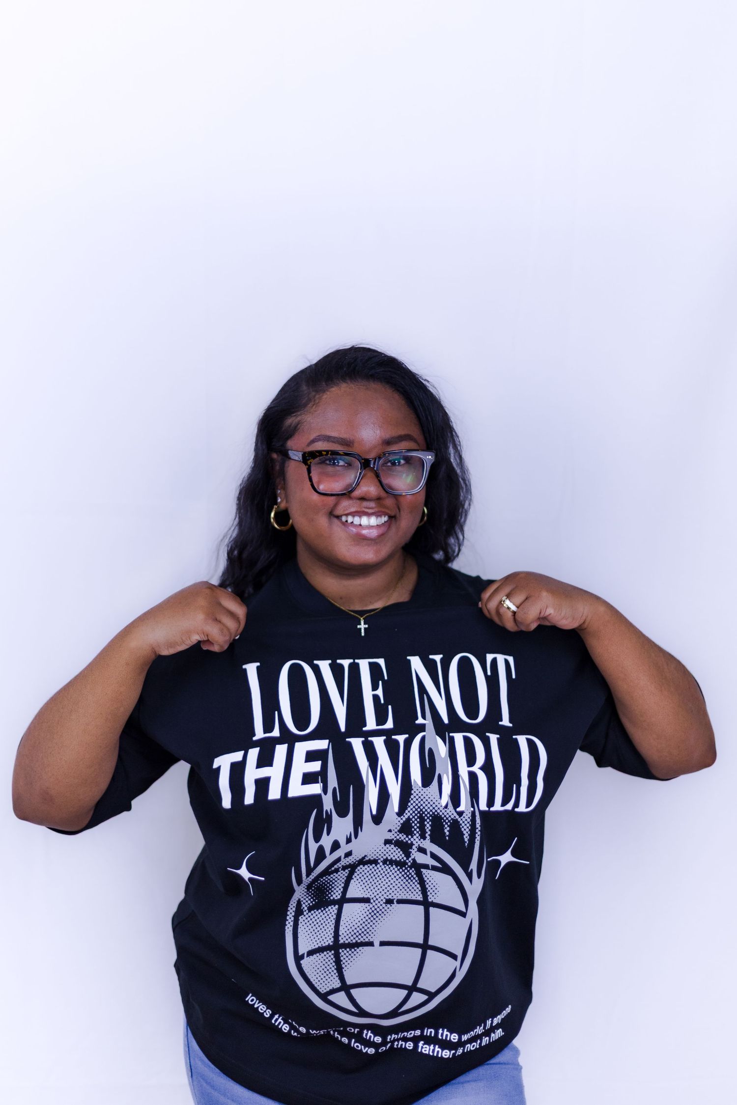 Smiling woman pulling her black Love Not The World graphic tee while wearing glasses.