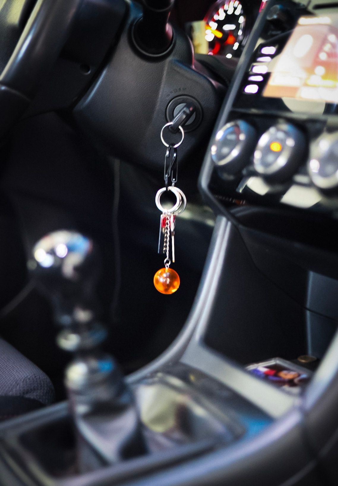 Dragon Ball Z orange crystal ball keychain hanging from car ignition with manual shifter visible.