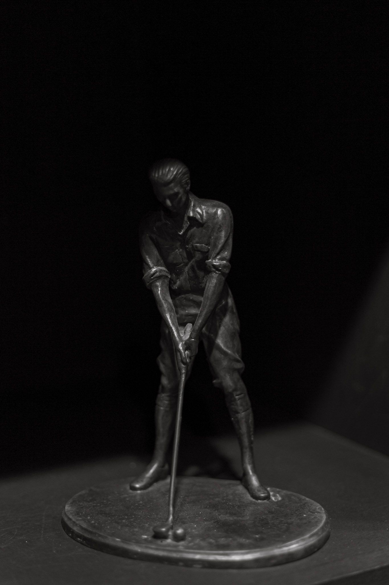 Vintage black metal golf figurine statue of a golfer mid-swing on a round base.