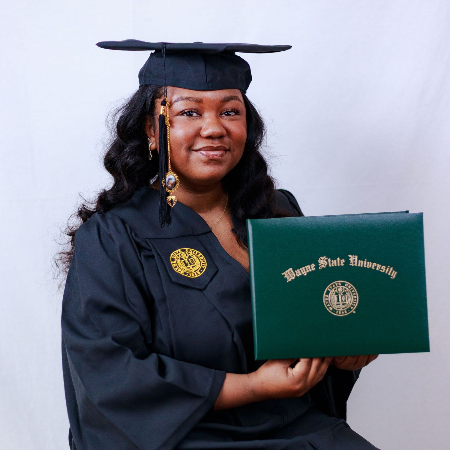 Graduate proudly holding Wayne State University diploma in green cover while wearing cap and gown.