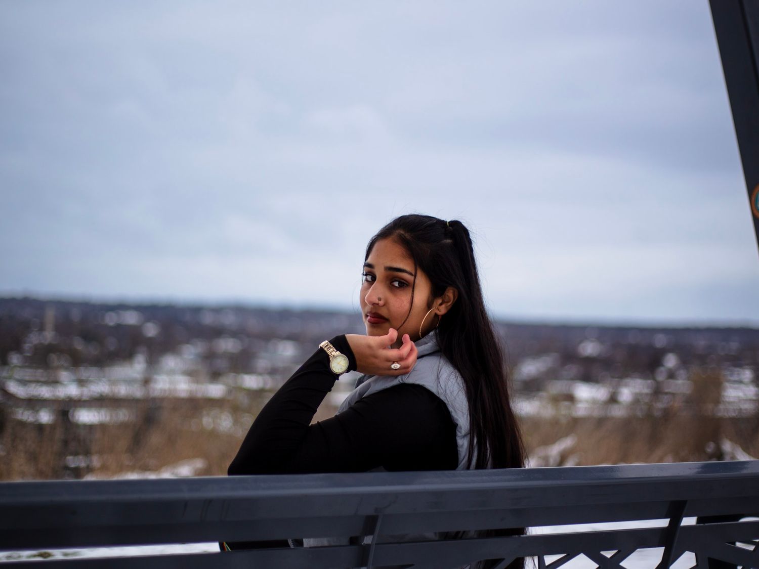 Young woman with ponytail on balcony overlooking snowy winter landscape under cloudy sky.