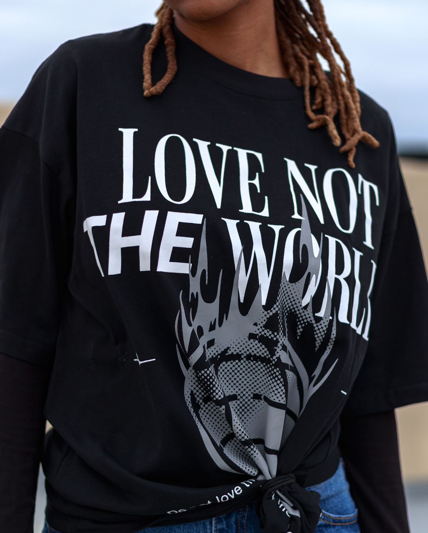 Detail shot of black 'Love Not The World' graphic tee featuring bold white typography and dark artistic design.