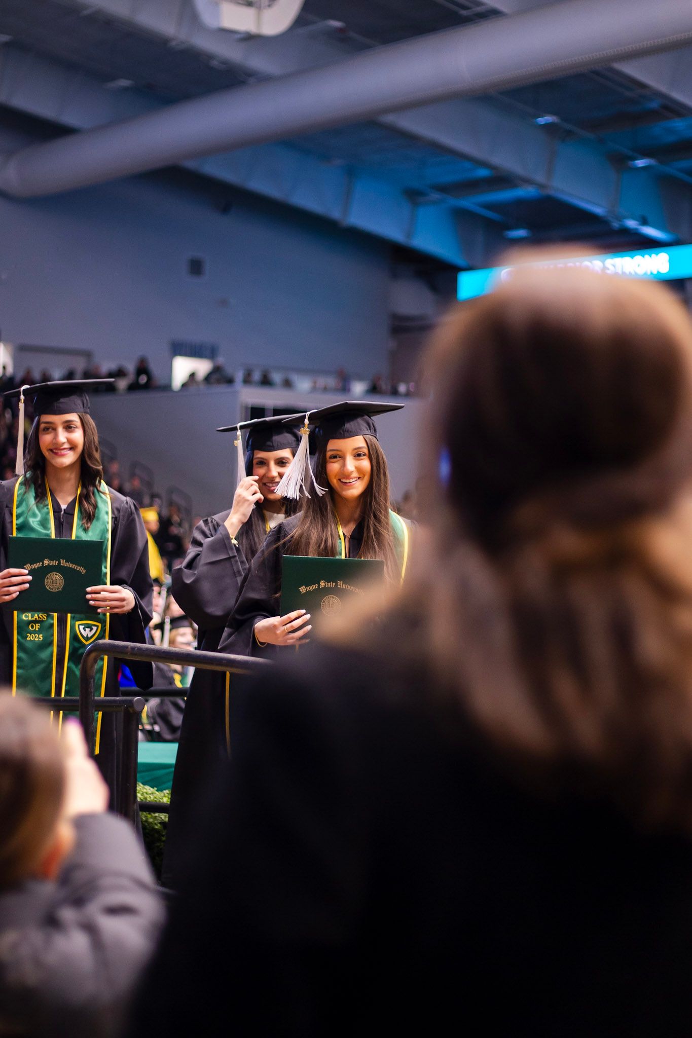 Two smiling female graduates hold diplomas in black caps and gowns at ceremony.
