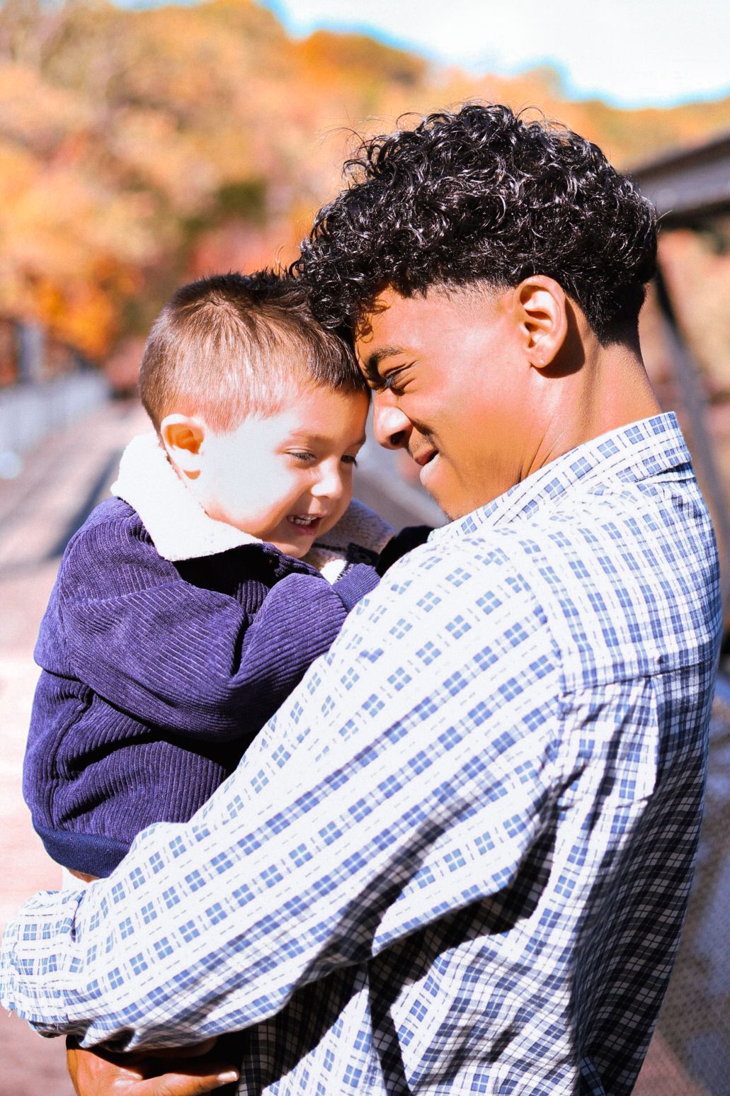 Loving father and smiling toddler son touching foreheads during fall family portrait outdoors.