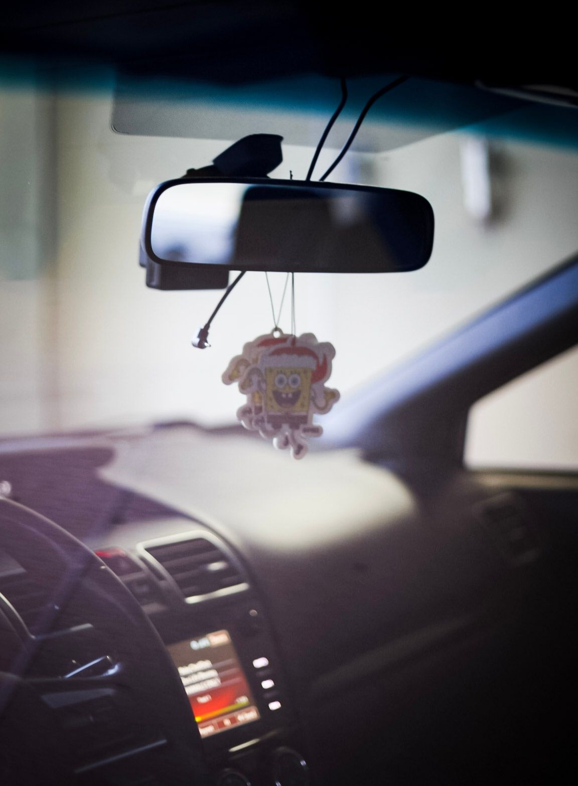 SpongeBob Christmas ornament air freshener hanging from rearview mirror inside a car interior.