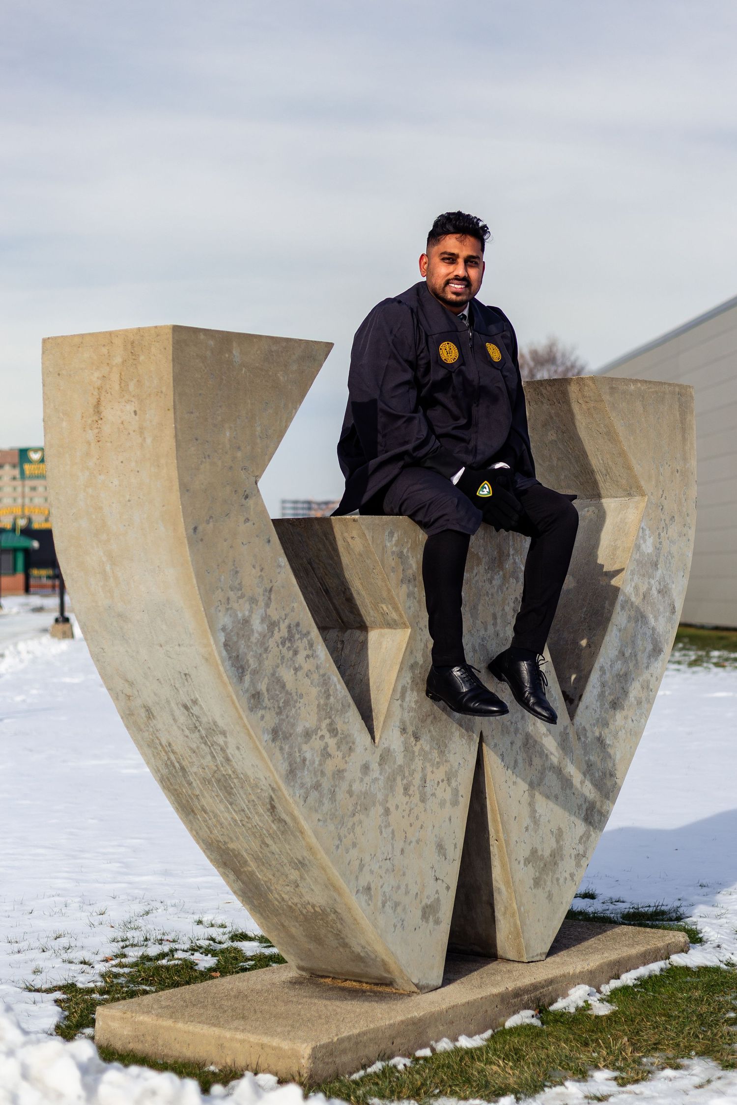 Graduate sitting atop large concrete Wayne State University W sculpture in winter snow.