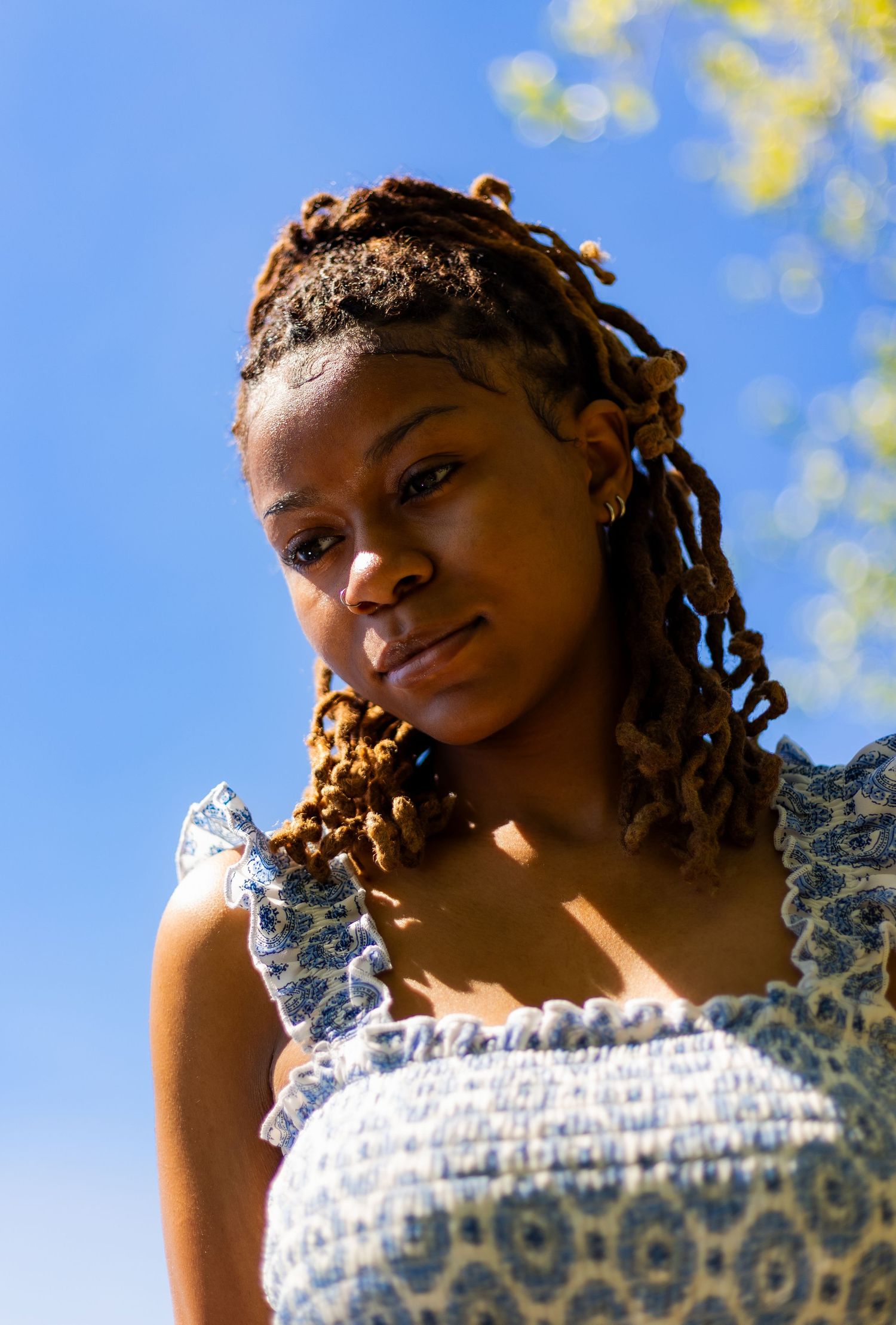 Low-angle portrait of young Black woman with locs against vivid blue sky outdoors.