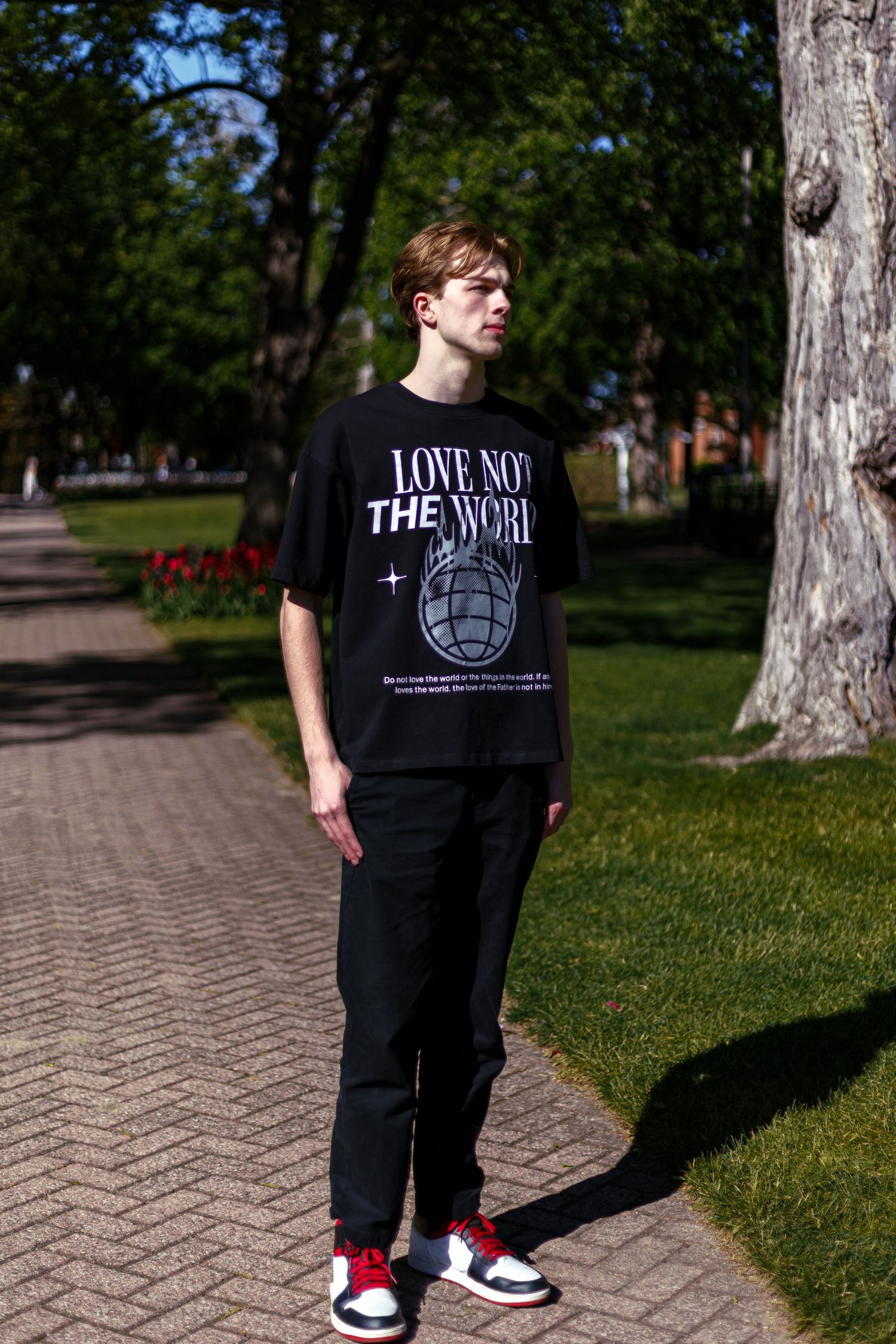 Young man standing on brick path wearing black Love Not The World tee with Jordan sneakers.