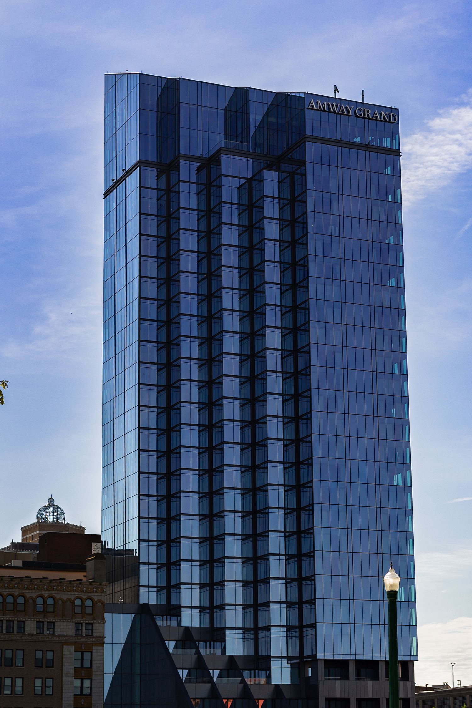 The Amway Grand Plaza Hotel tower, a modern glass skyscraper, rises against a blue sky in Grand Rapids, Michigan.