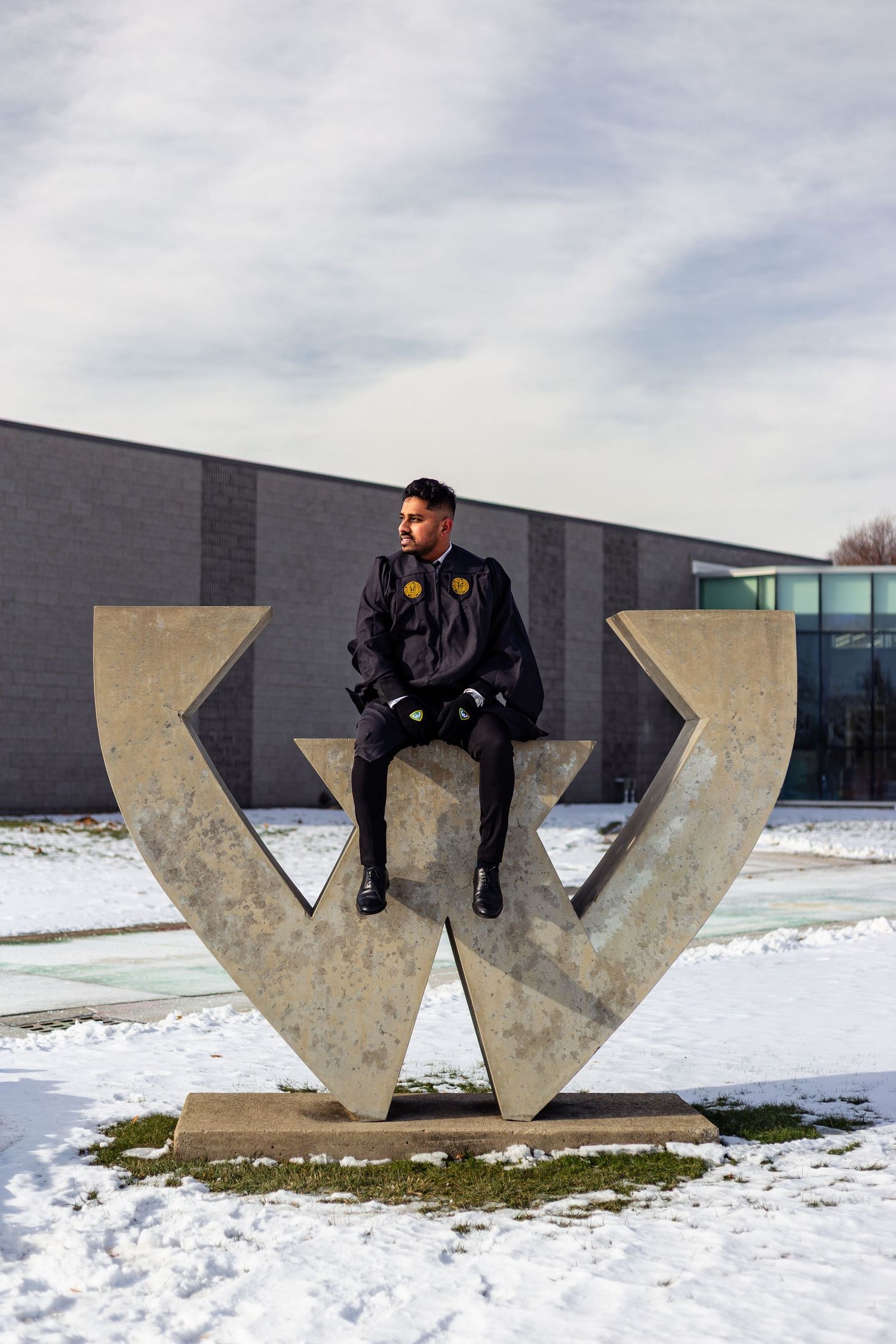 Wayne State graduate sitting on large concrete W campus sculpture under cloudy winter sky.