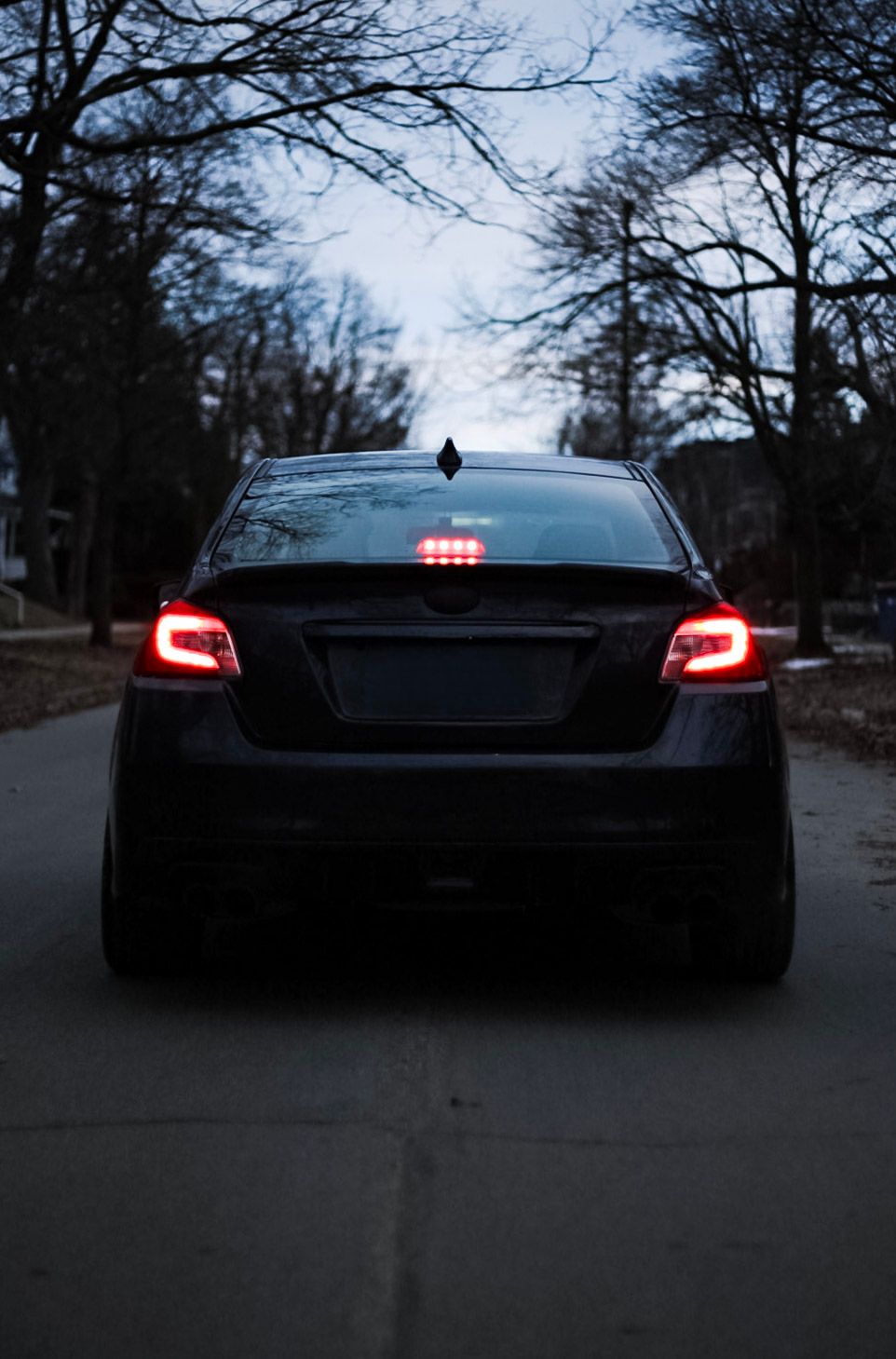 Rear view of a black Subaru with bright red taillights glowing on a quiet dark street.