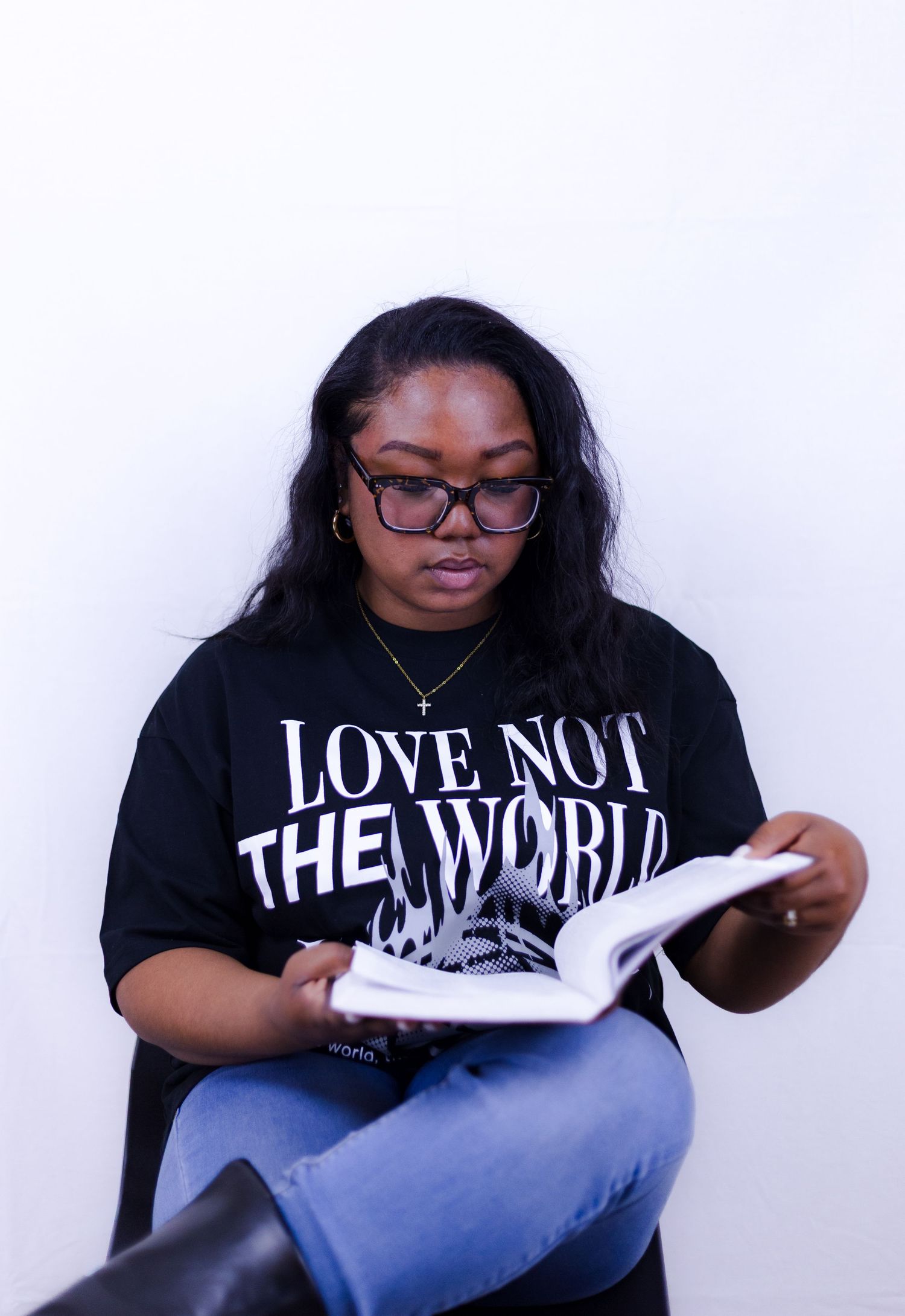 Woman reading Bible wearing black Love Not The World graphic tee, glasses, and jeans.
