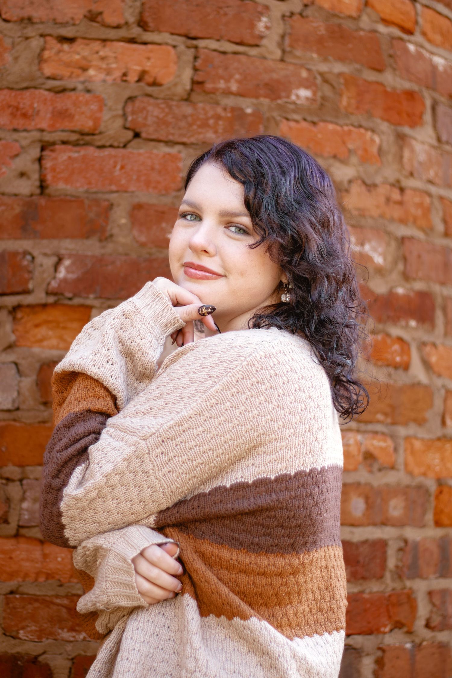 Sequence showing person wrapping themselves in cozy beige sweater against rustic brick wall background.