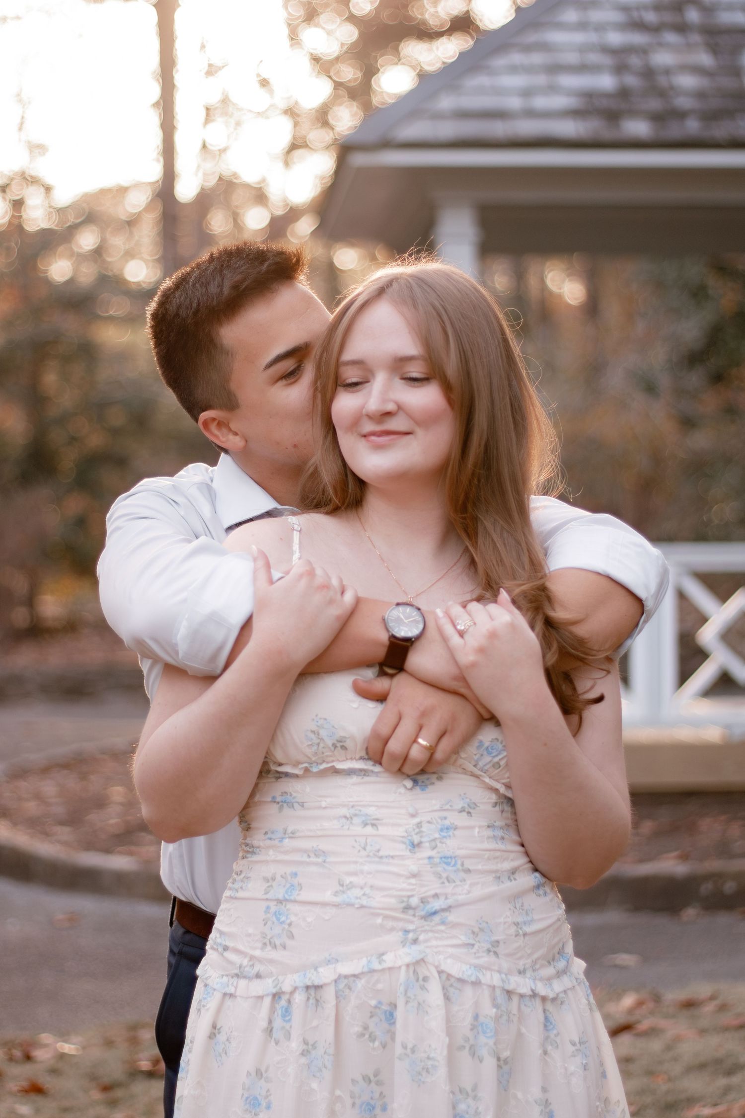 A romantic couple embraces at sunset in front of a white gazebo during a photo session.