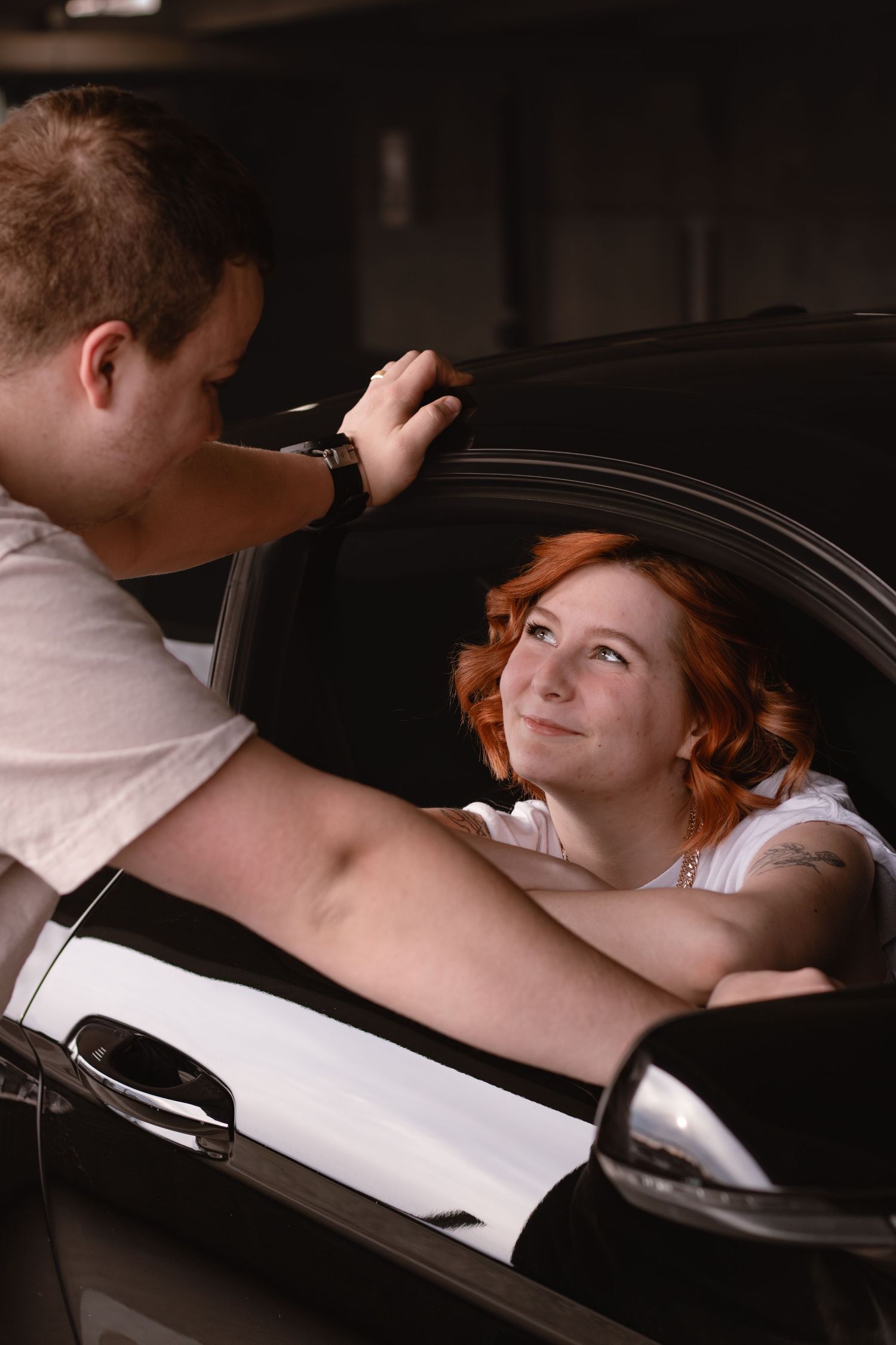 Someone takes a photo of a person with red hair resting in a car window during a photo shoot.