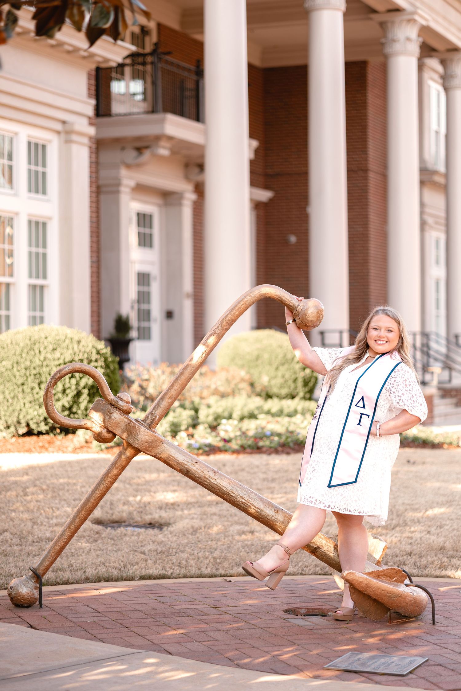 Someone poses with a large decorative anchor statue outside a columned building.