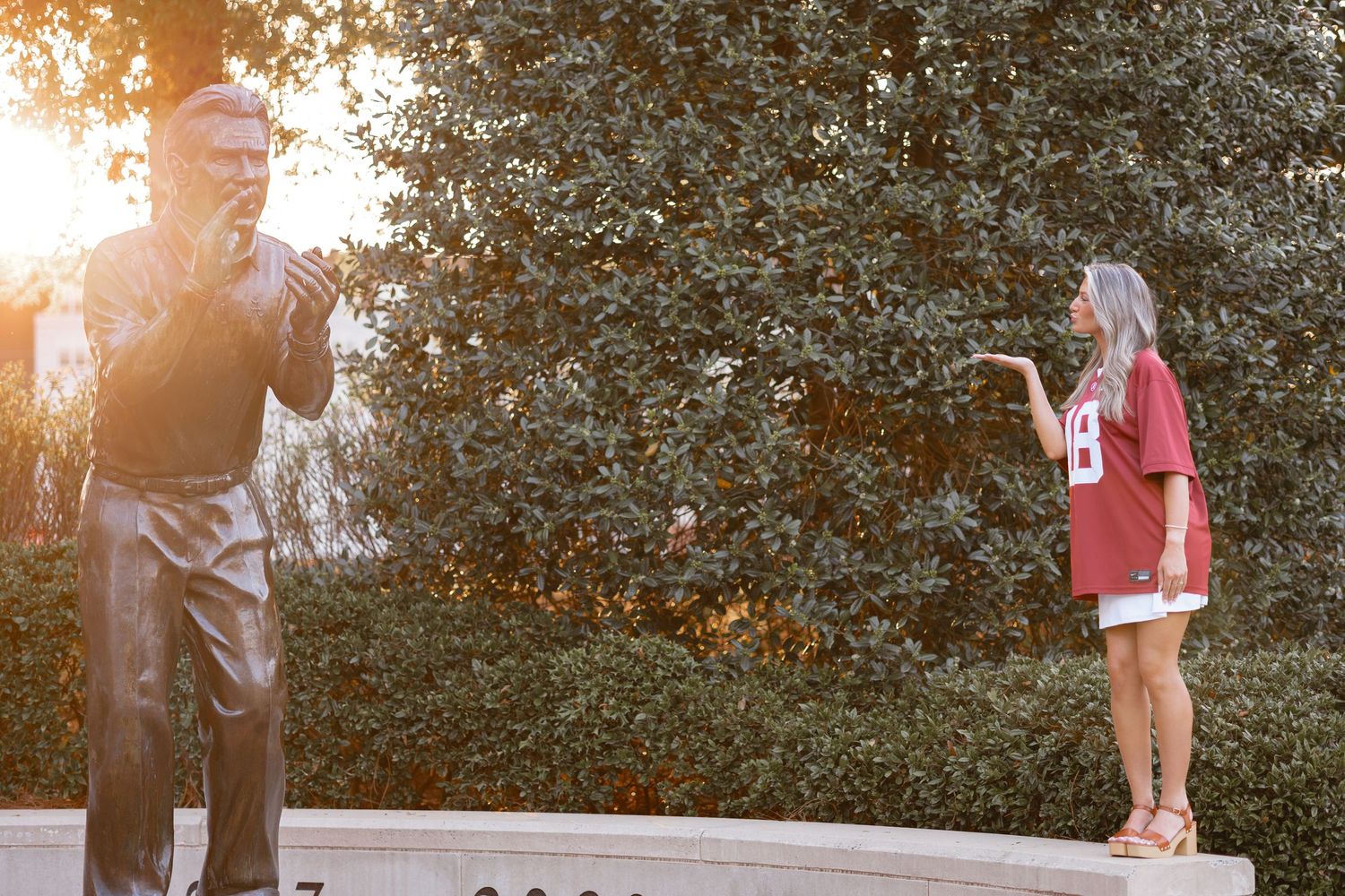 A person stands with a statue of Nick Saban.