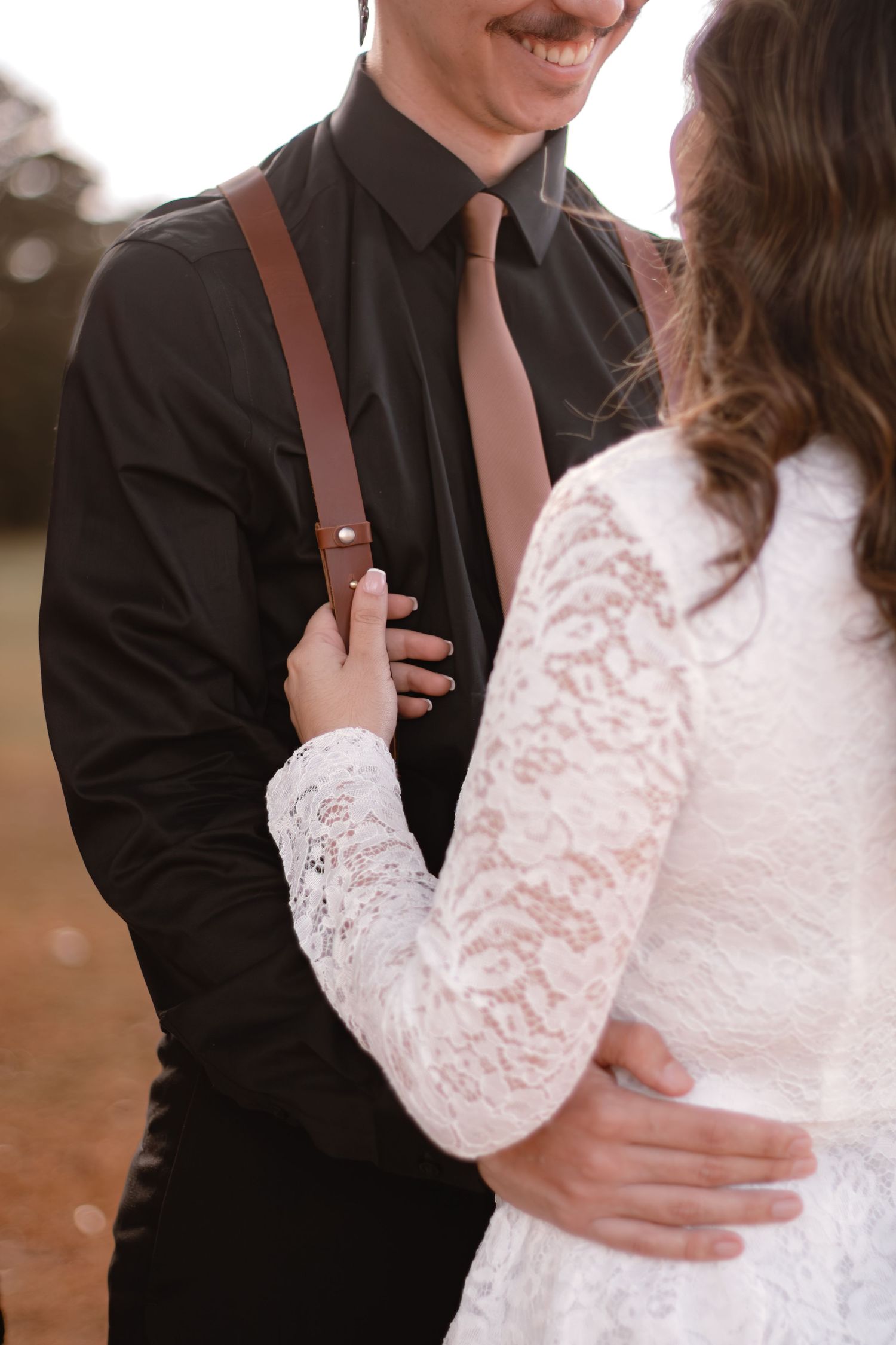 A close-up shot of a couple in wedding attire with the groom wearing suspenders and a dark shirt.