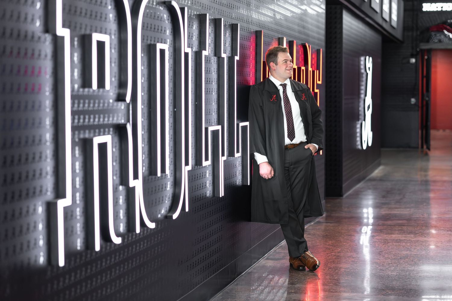 Man in suit leaning against illuminated TRON signage in a modern corridor.
