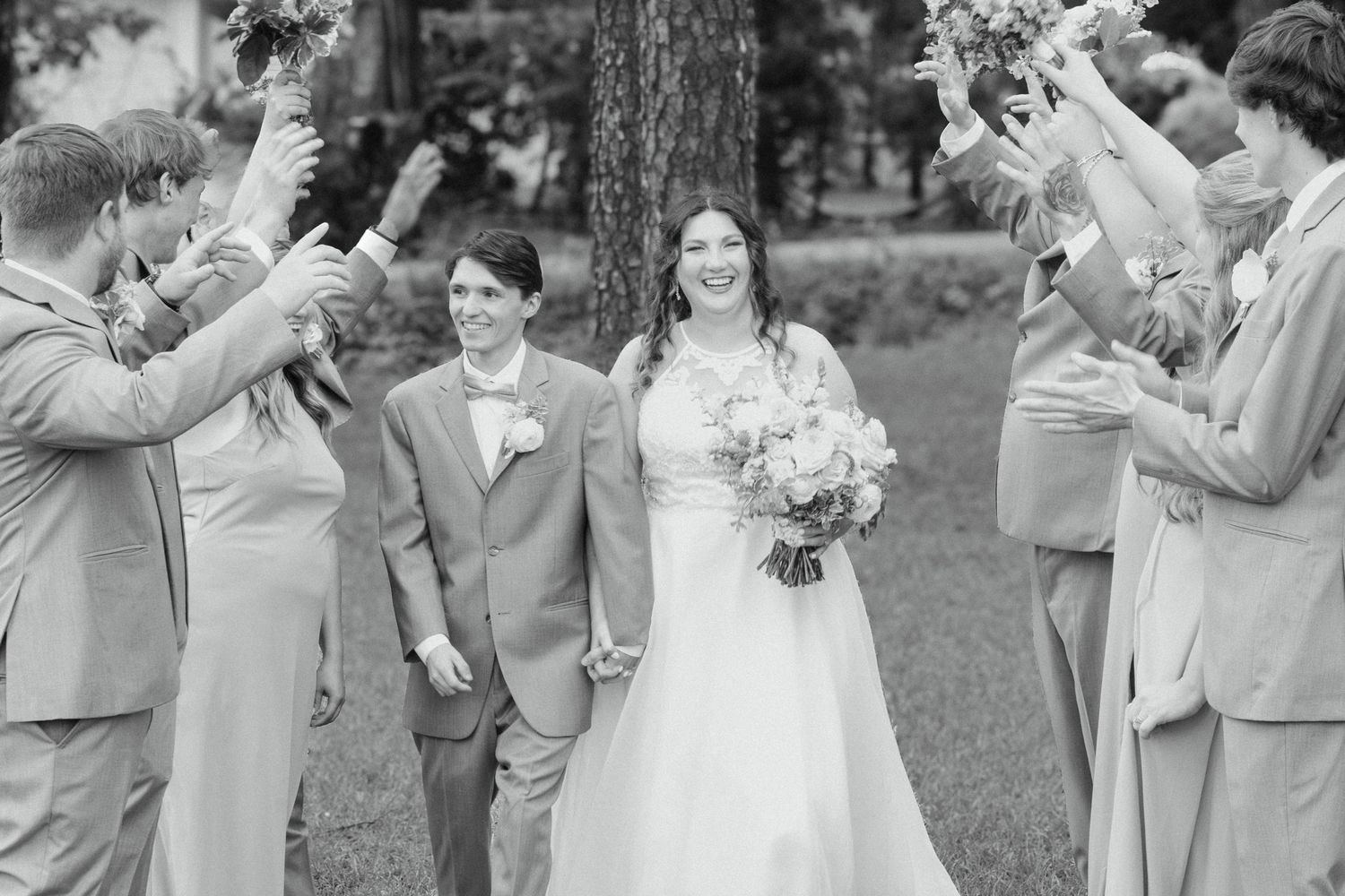 Black and white photo of newlyweds walking through cheering wedding party outdoors.