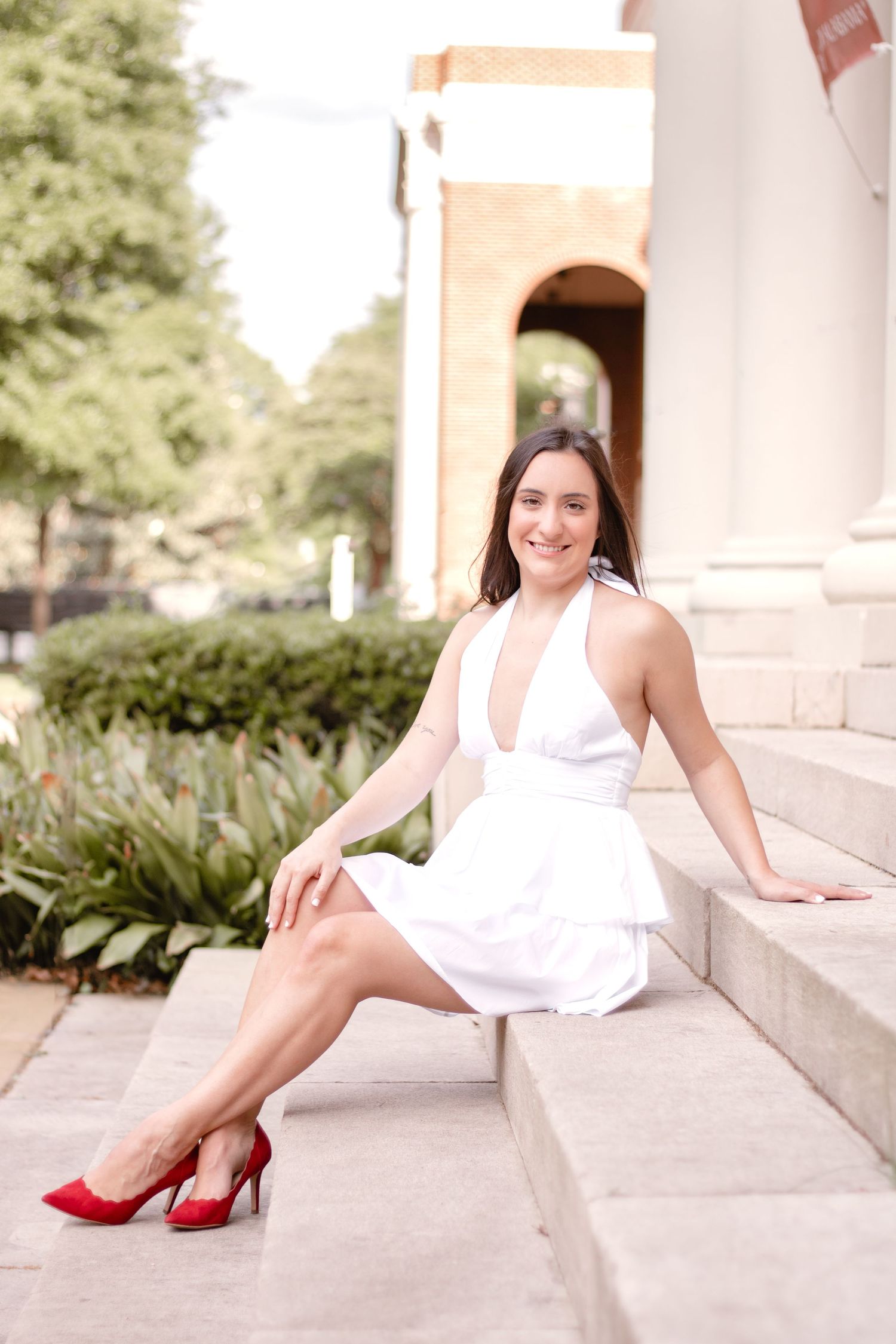A person in a white dress and red heels poses elegantly on stone steps.