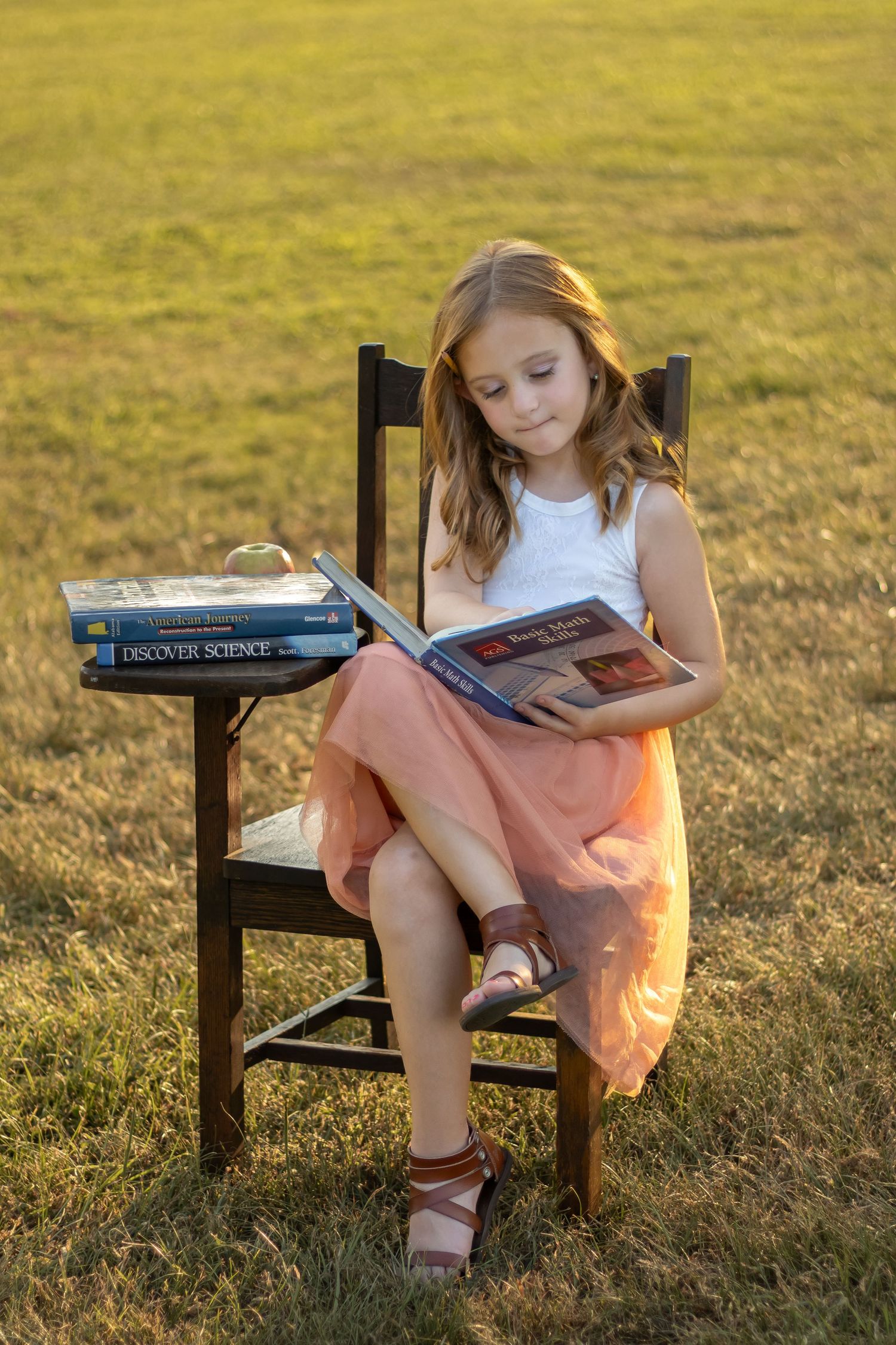 A reader enjoys a book while sitting on a wooden chair in a sunlit meadow at golden hour.