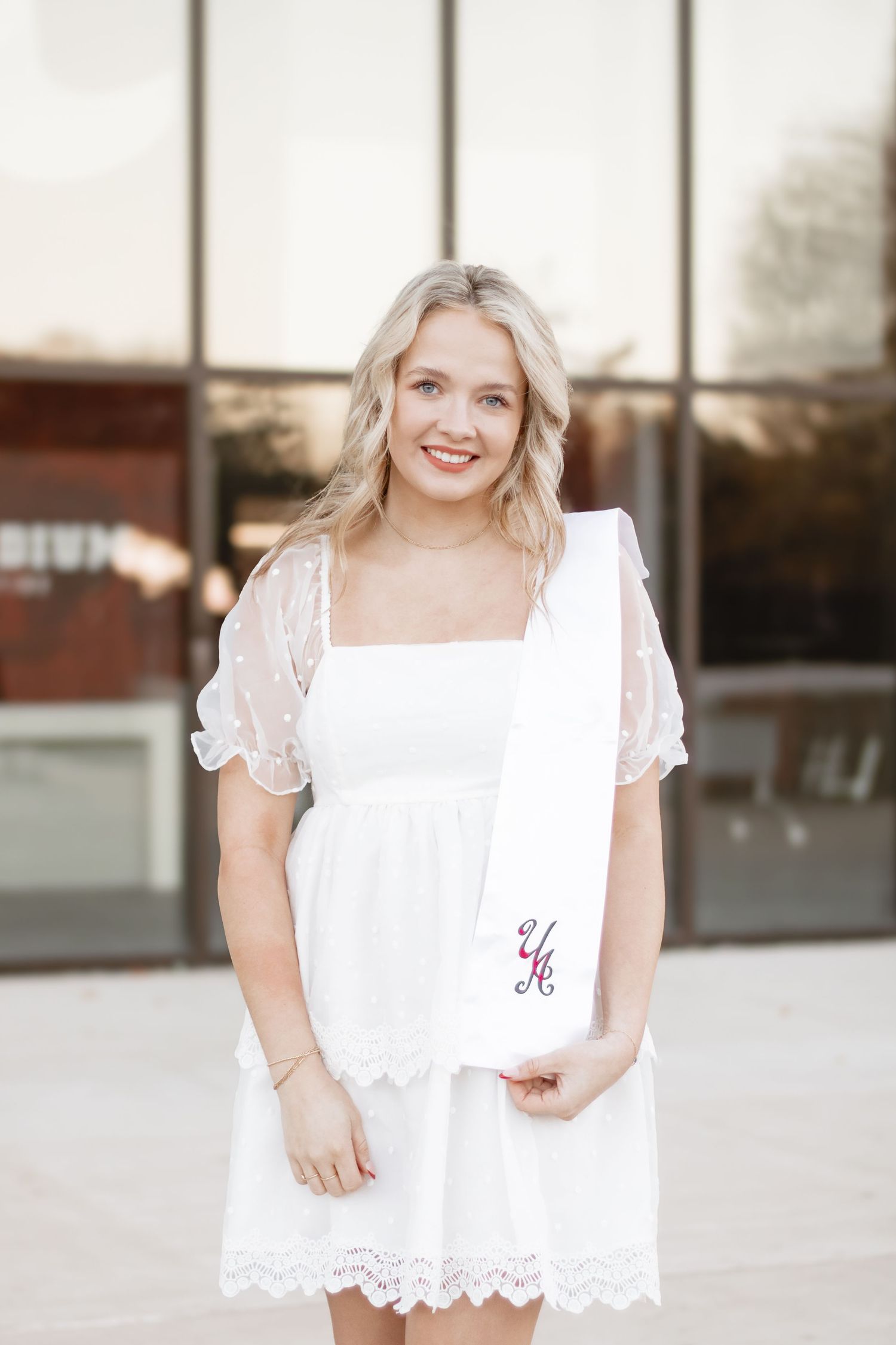 A person wearing a white lace dress with sheer short sleeves stands outside a building.