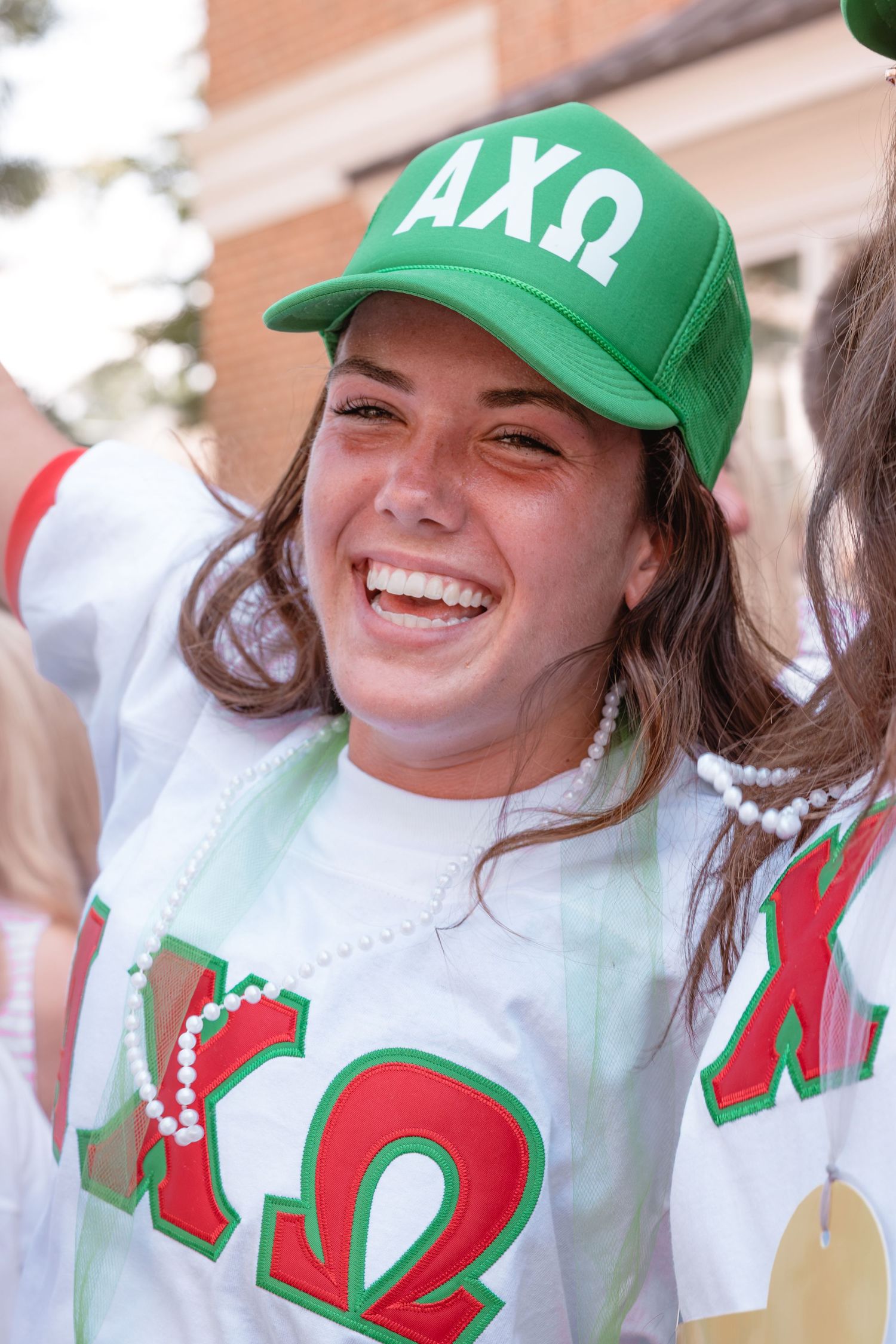 A student wearing a green AXO baseball cap and white Greek letter shirt smiles during bid day.