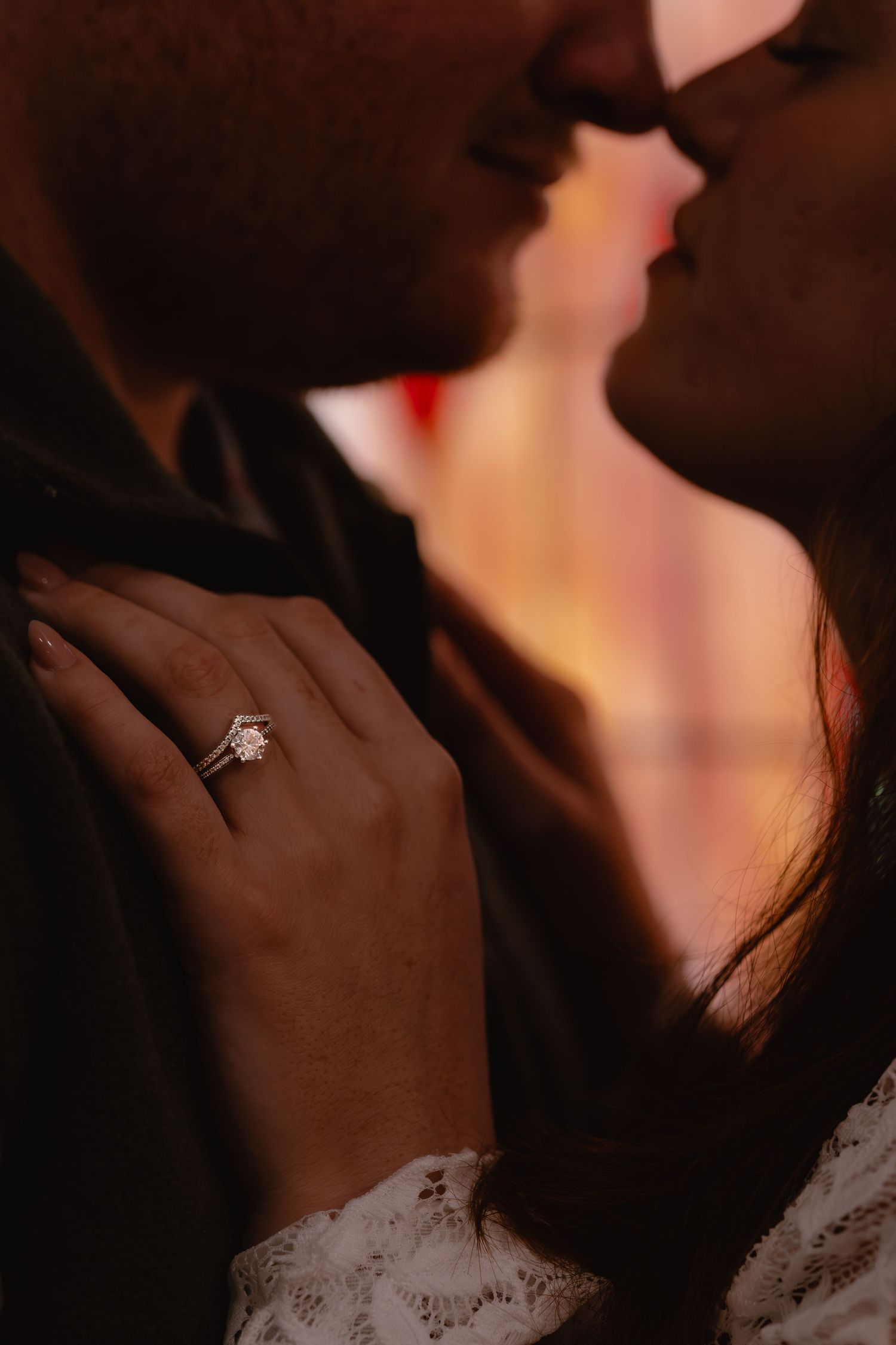 Close-up silhouette of a couple in an intimate moment with an engagement ring visible on a hand.