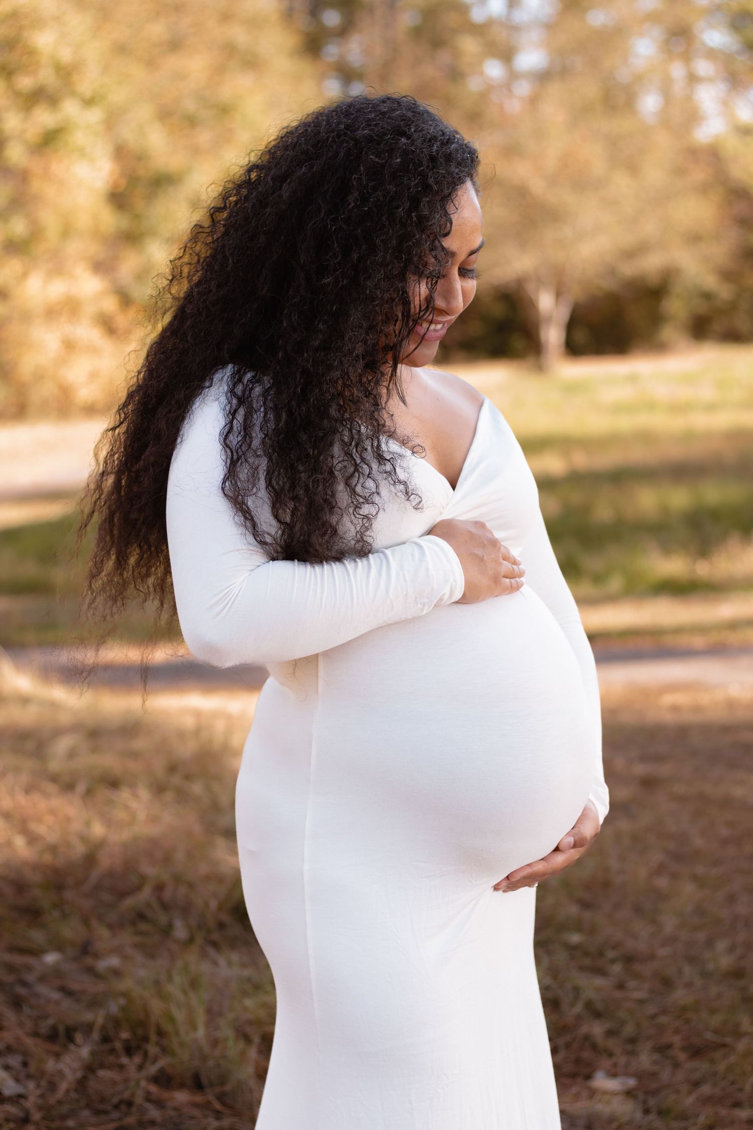 A maternity portrait of a person in a white fitted dress during golden hour.