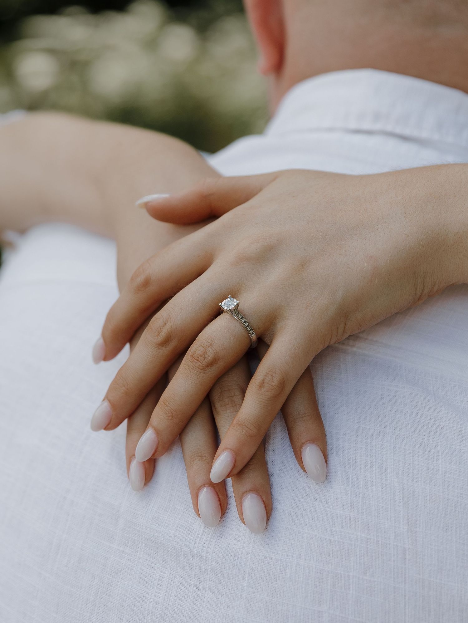 Close-up of hands with freshly manicured nails and engagement ring resting on white fabric.
